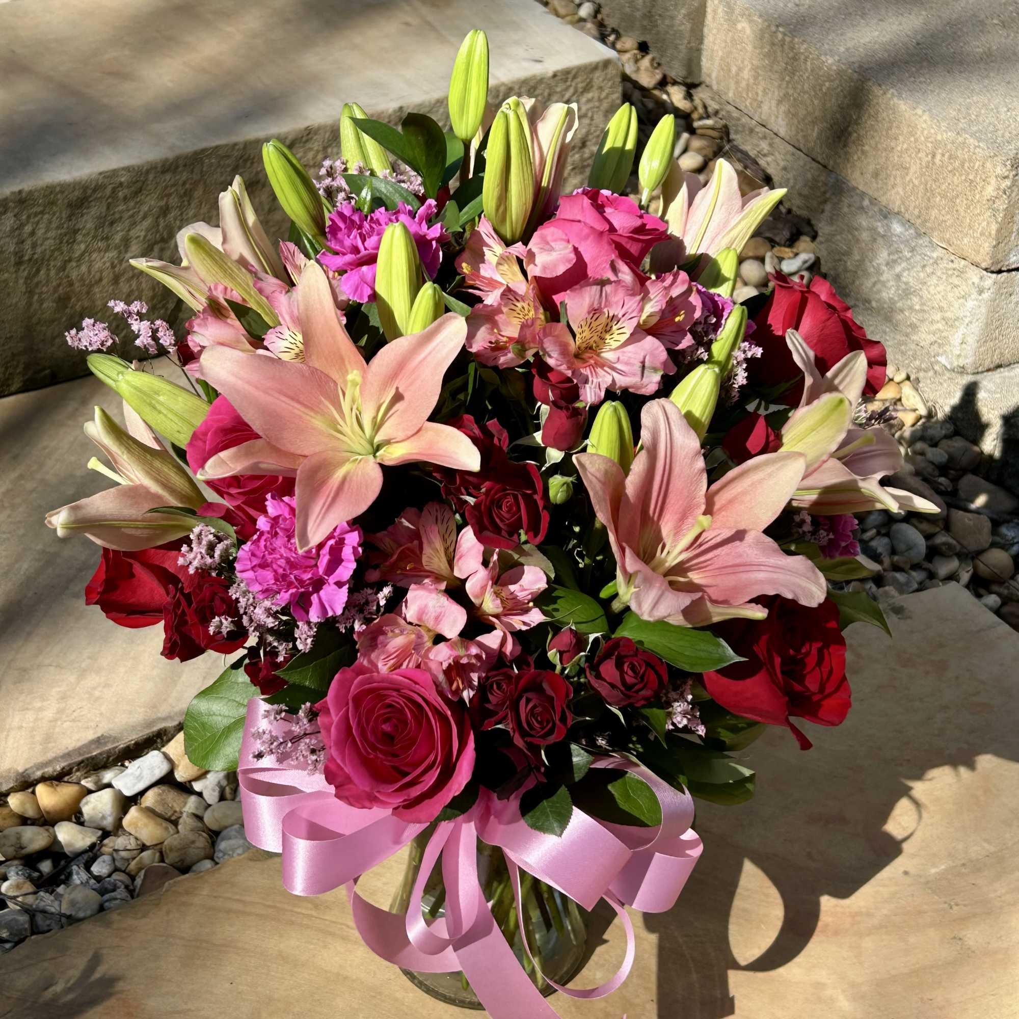 A pink and red bouquet of roses, lilies, carnations, spray roses, and