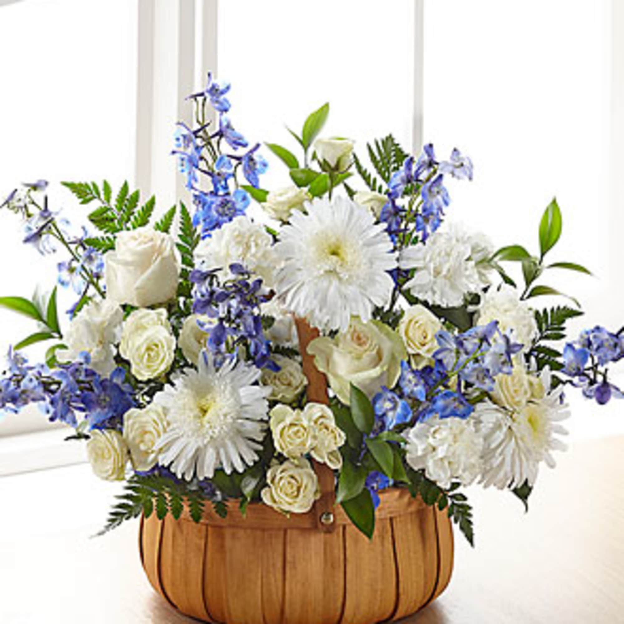 This basket arrangement has blue and white flowers such as delphinium, spray