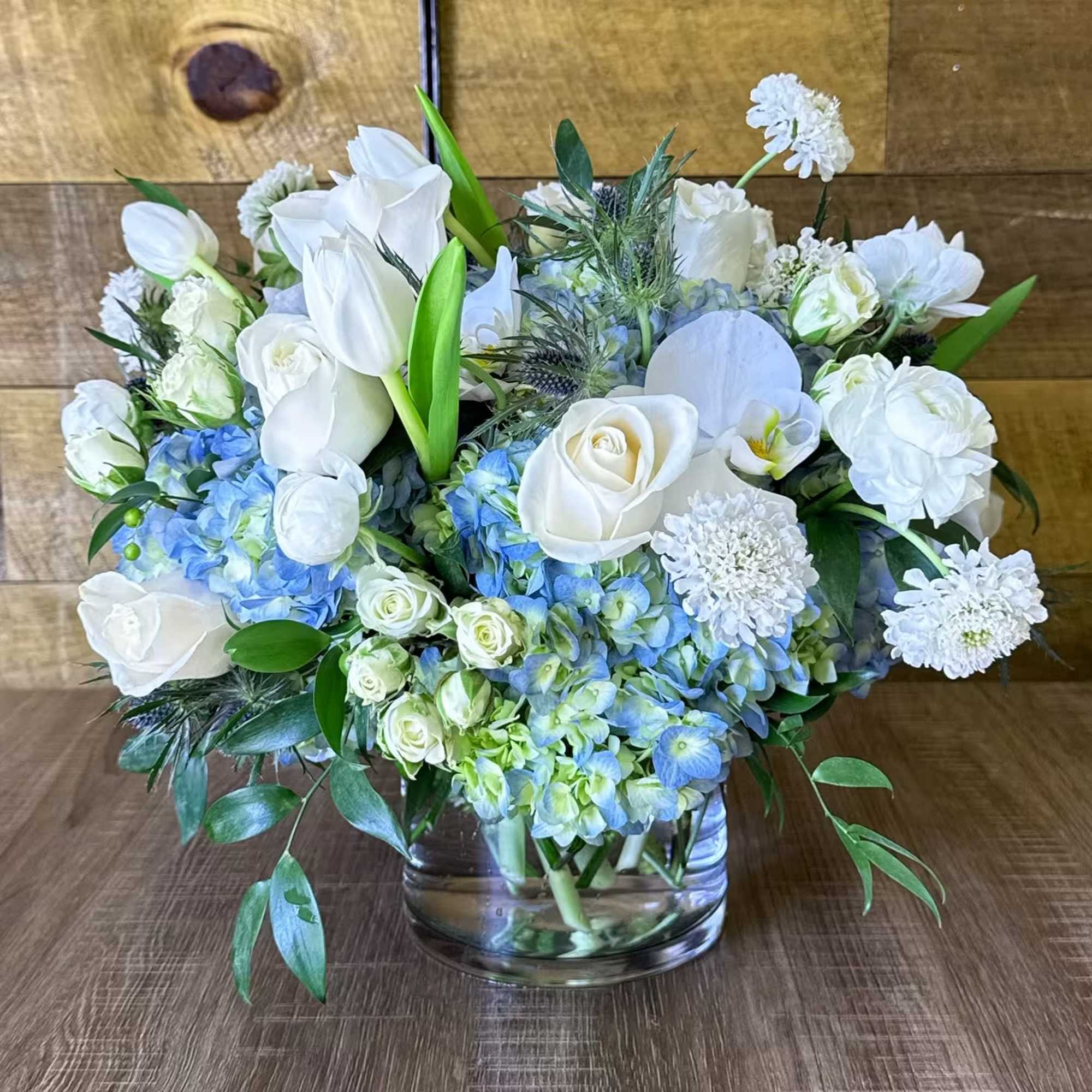 Beautiful round arrangement with a mixture of roses, blue hydrangeas, spray roses