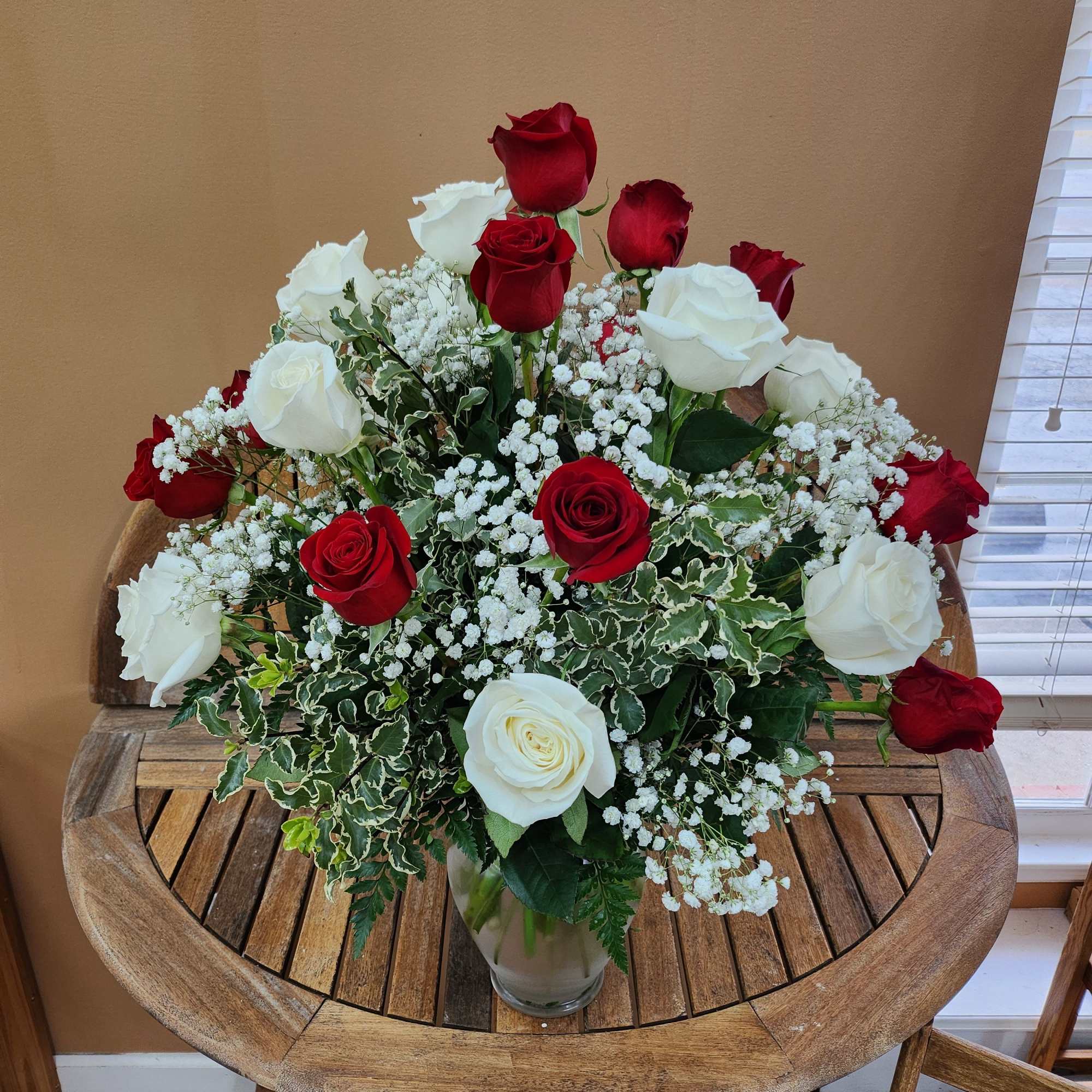 2 dozen red and white roses arranged in a vase with greens