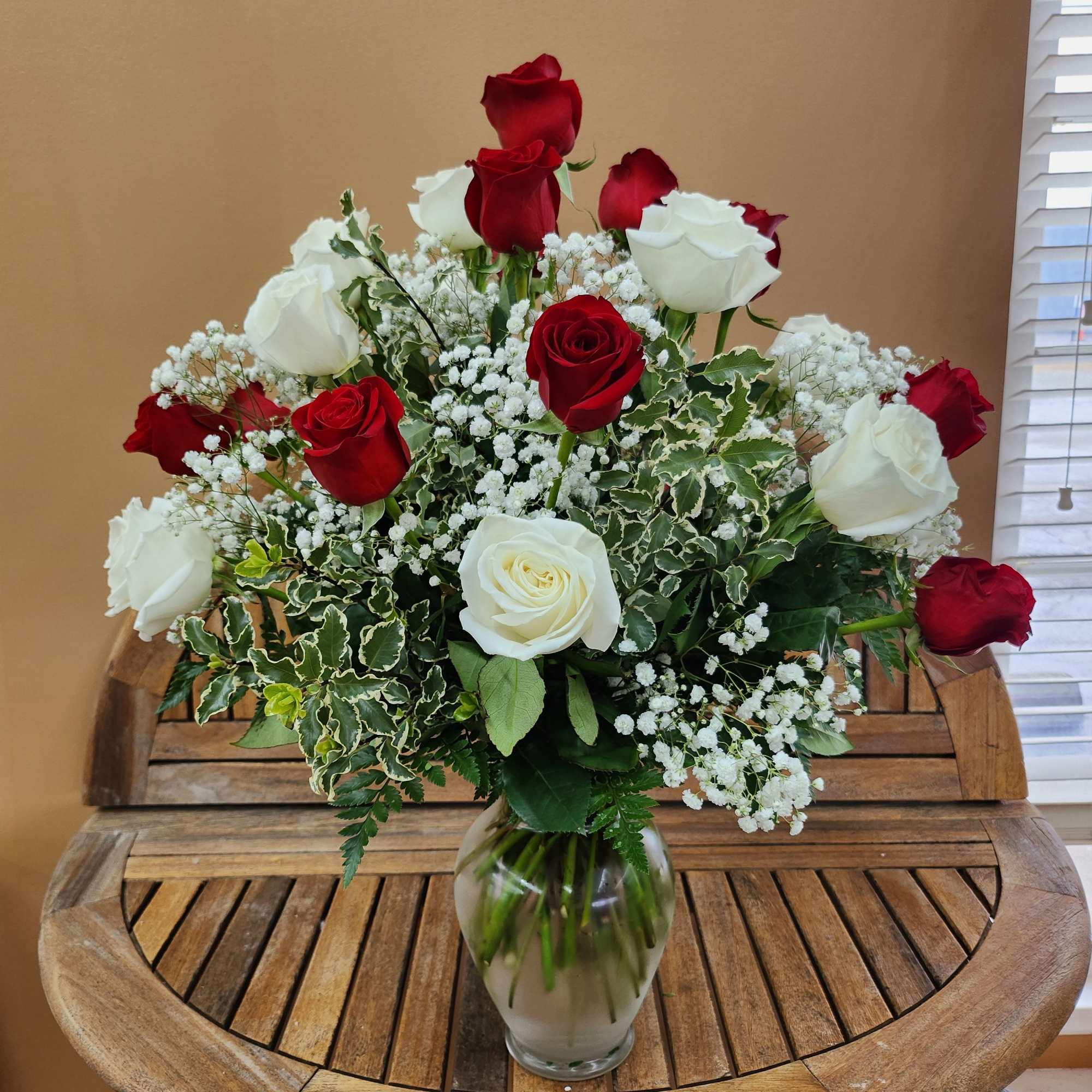 2 dozen red and white roses arranged in a vase with greens