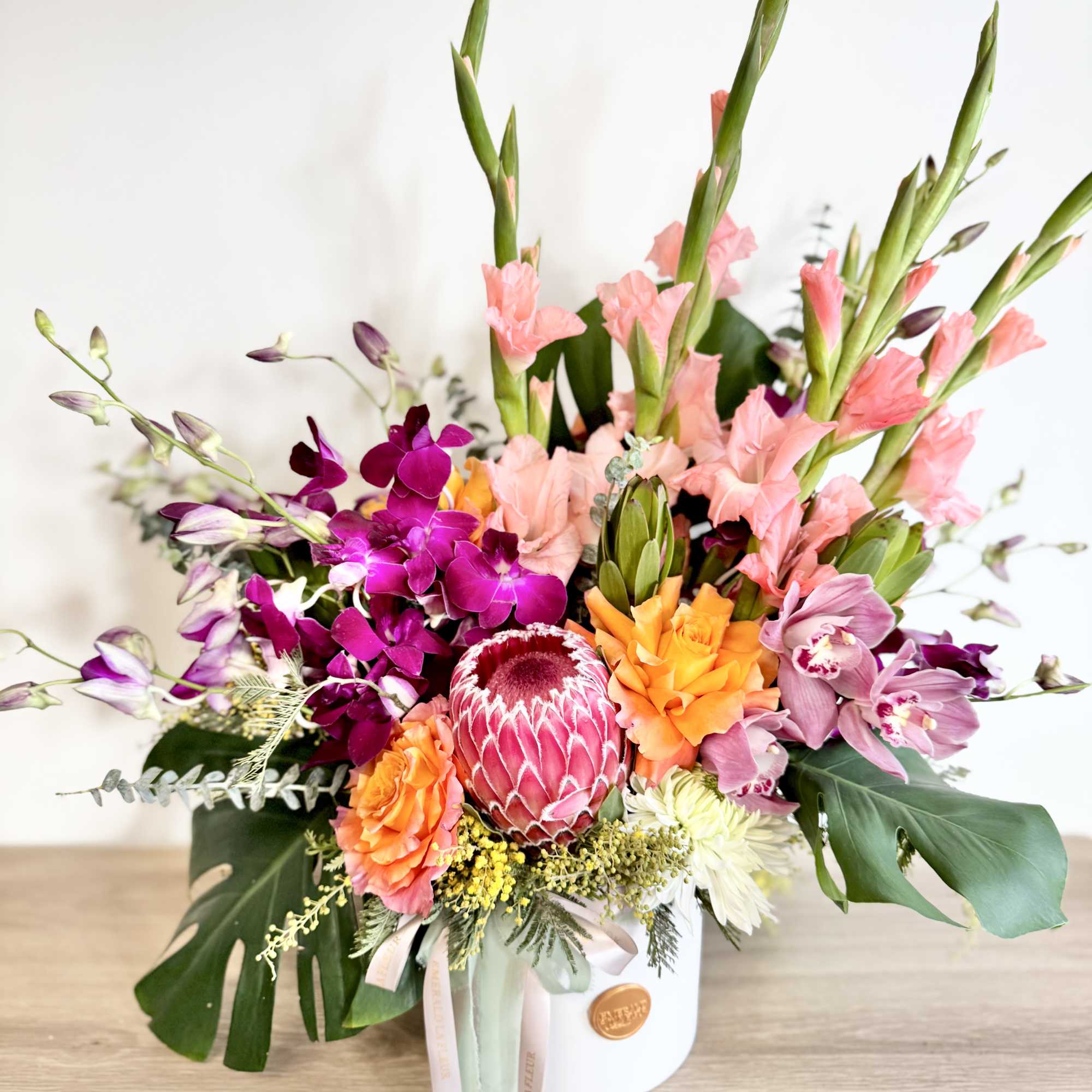 A lush, tropical inspired arrangement featuring vibrant blooms and bold textures. Each