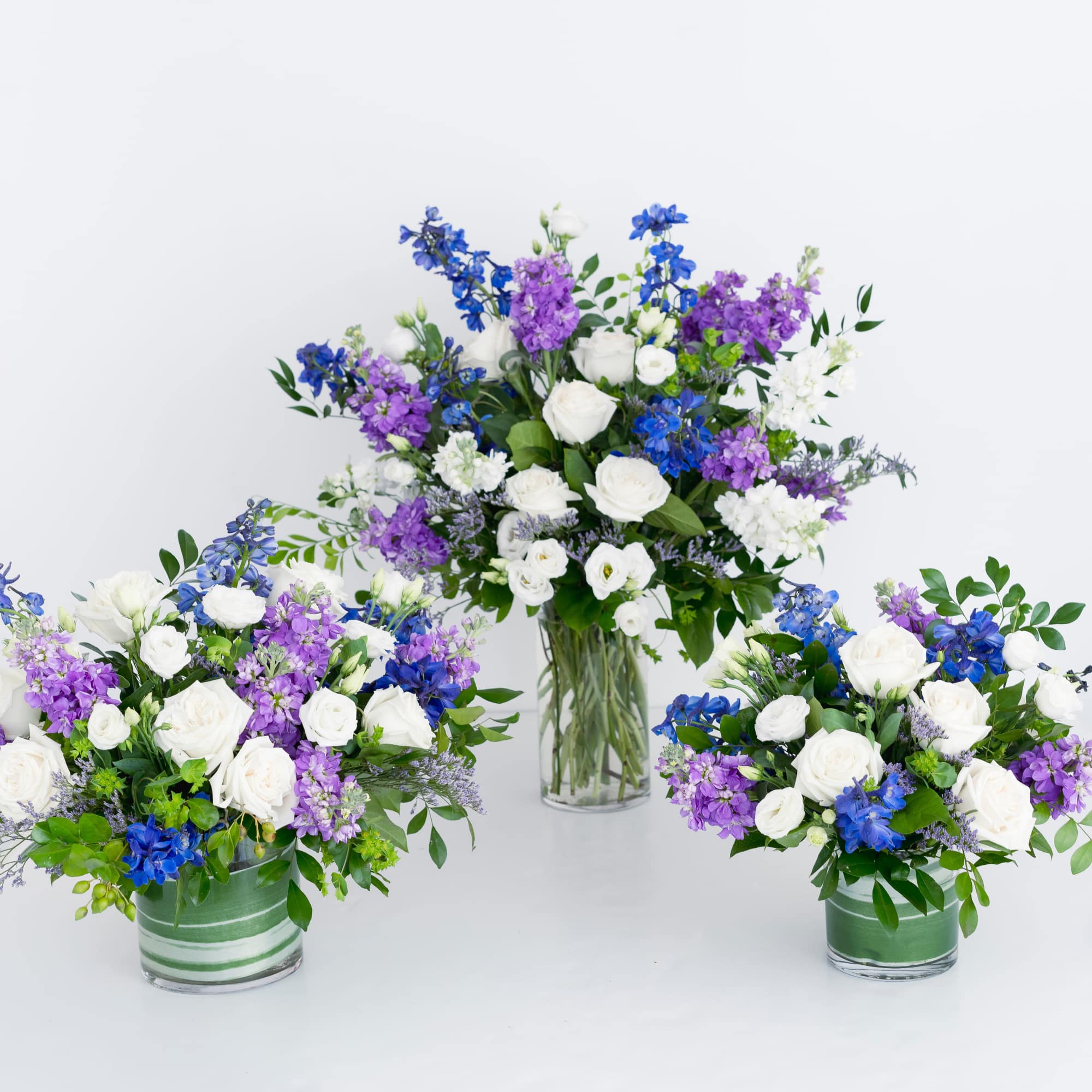 A low leaf-lined cylinder filled with roses, Stock, Lisianthus and Delphinium -