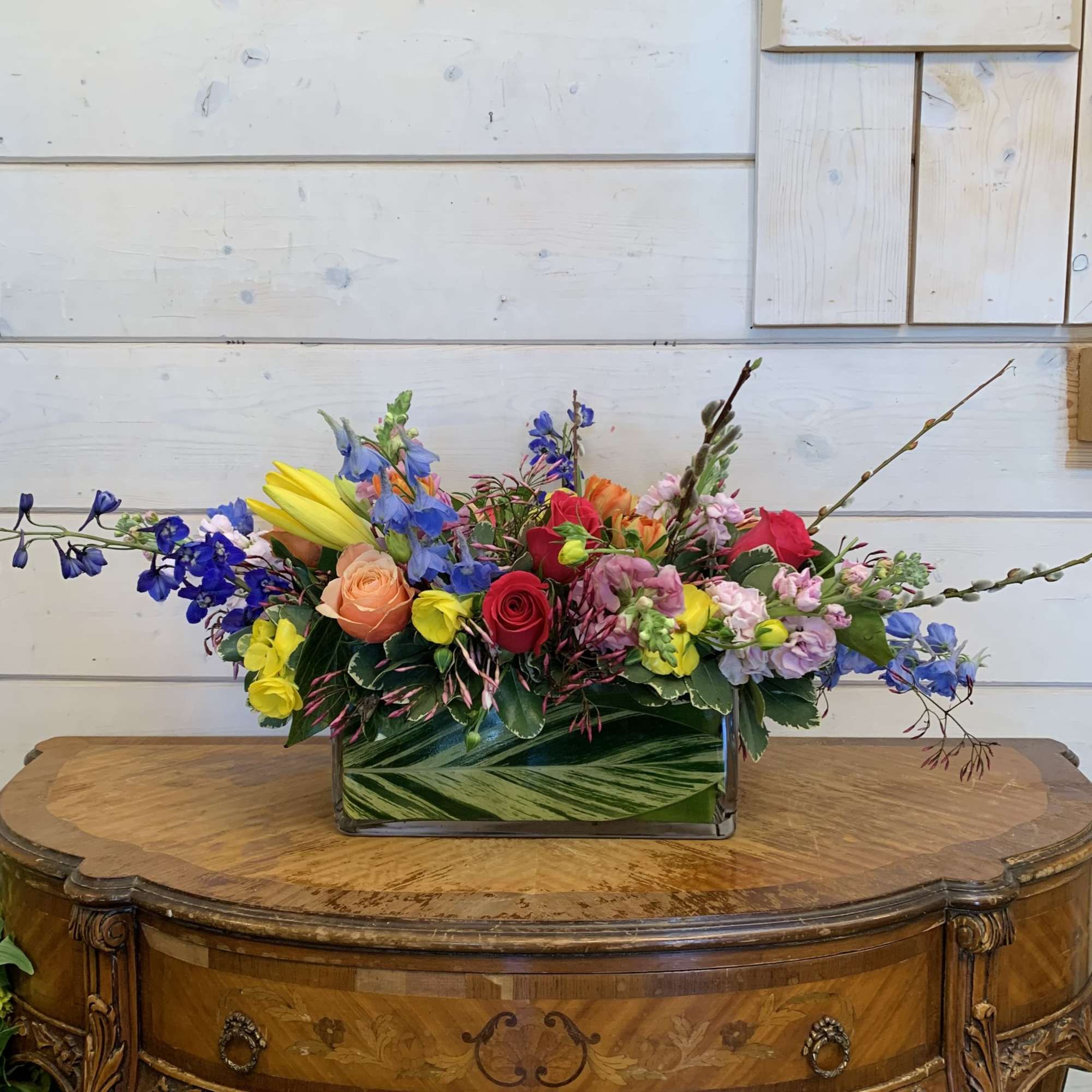 Pink and apricot roses, blue delphinium, yellow lily, butterfly ranunculus, orange tulips