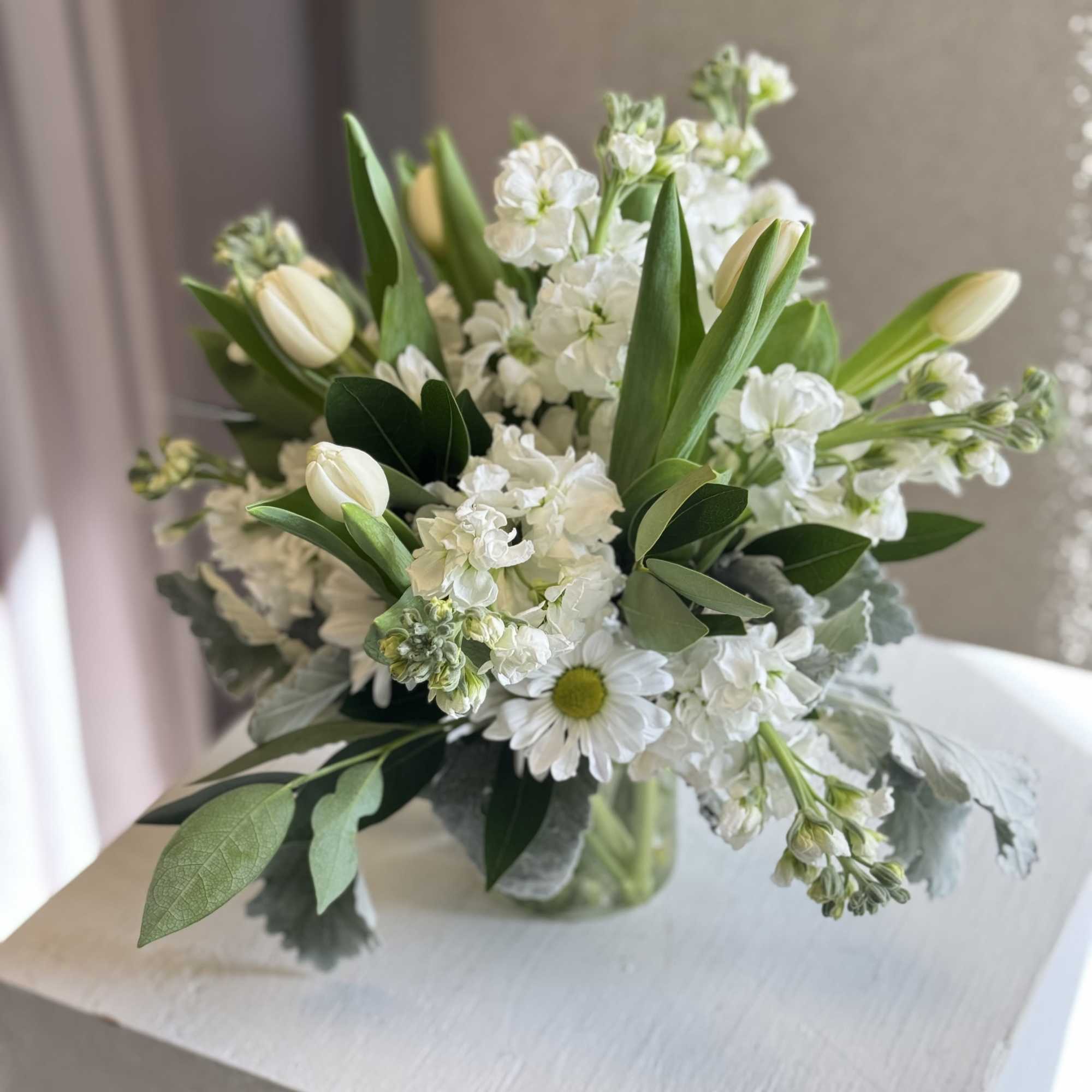 A fresh and timeless white floral arrangement featuring soft tulips, delicate stock