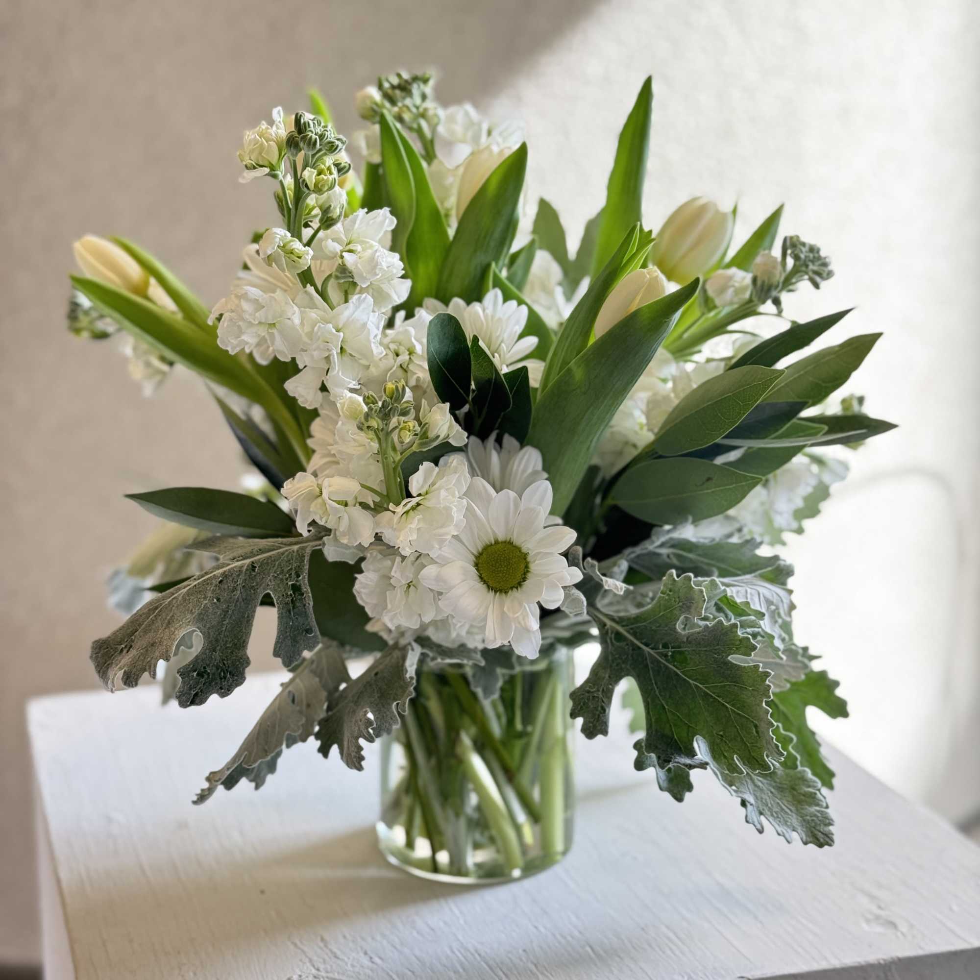 A fresh and timeless white floral arrangement featuring soft tulips, delicate stock
