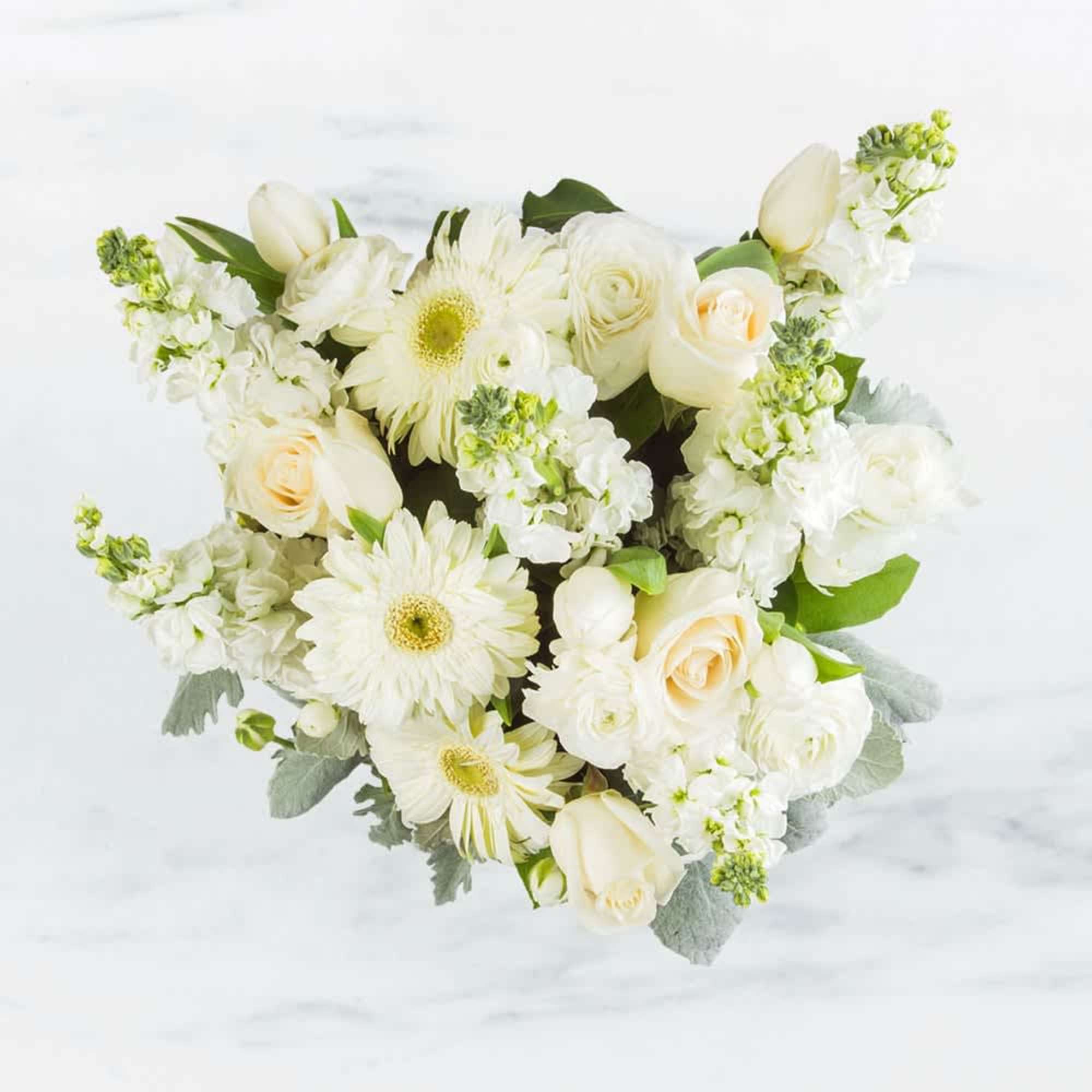 This arrangement contains gerbera daisies, roses, tulips, stock, and other seasonal blooms.
