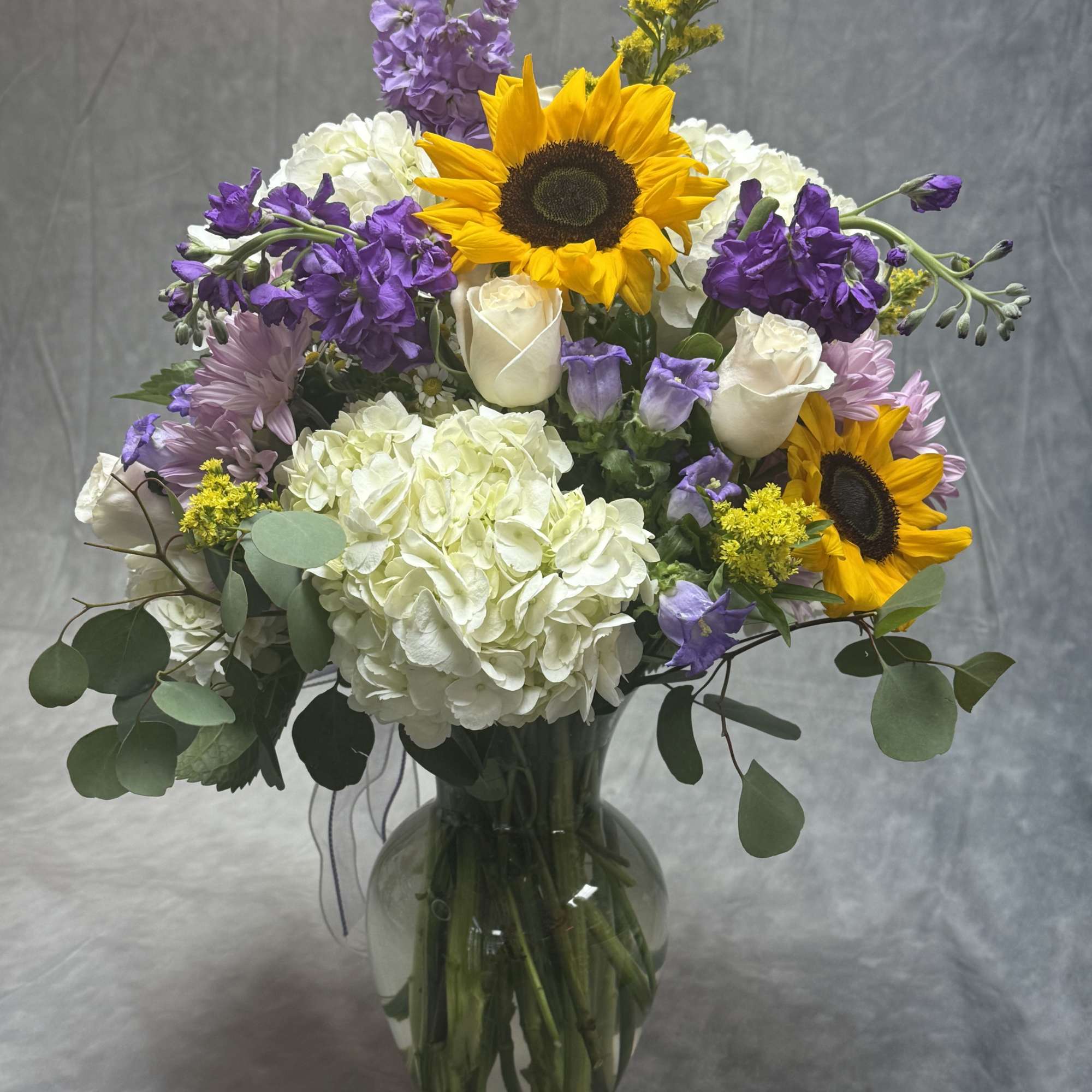 Golden sunflowers shine alongside white hydrangeas, roses, and cheerful daisies, accented with
