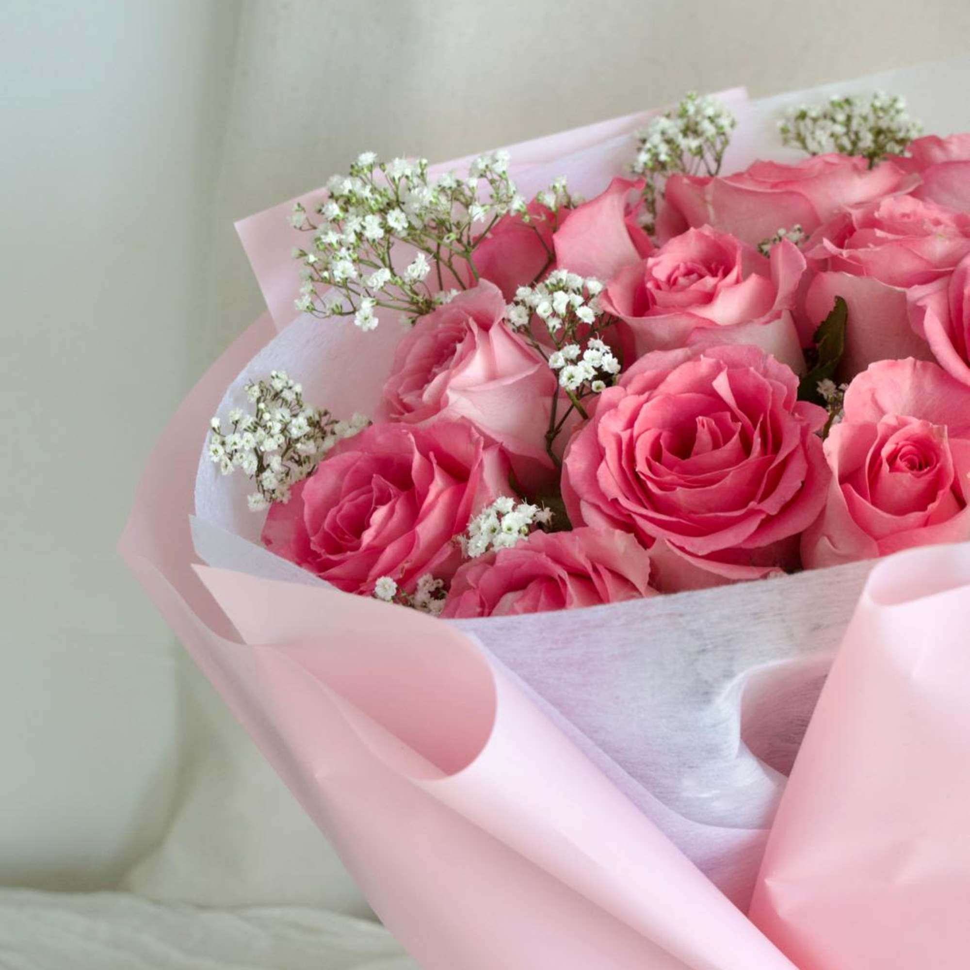 A round bouquet of roses and baby's breath, wrapped in pink paper.