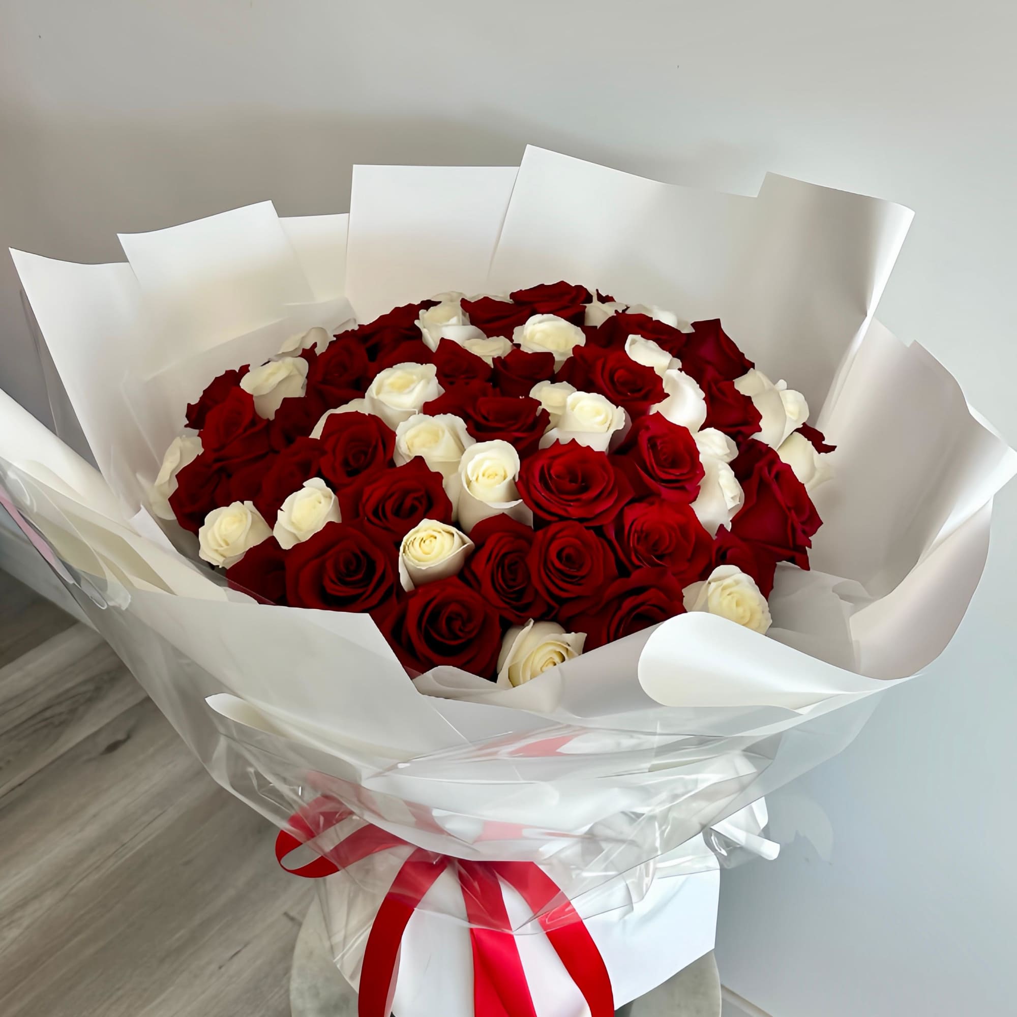 A round bouquet of 100 red and white roses, wrapped in white