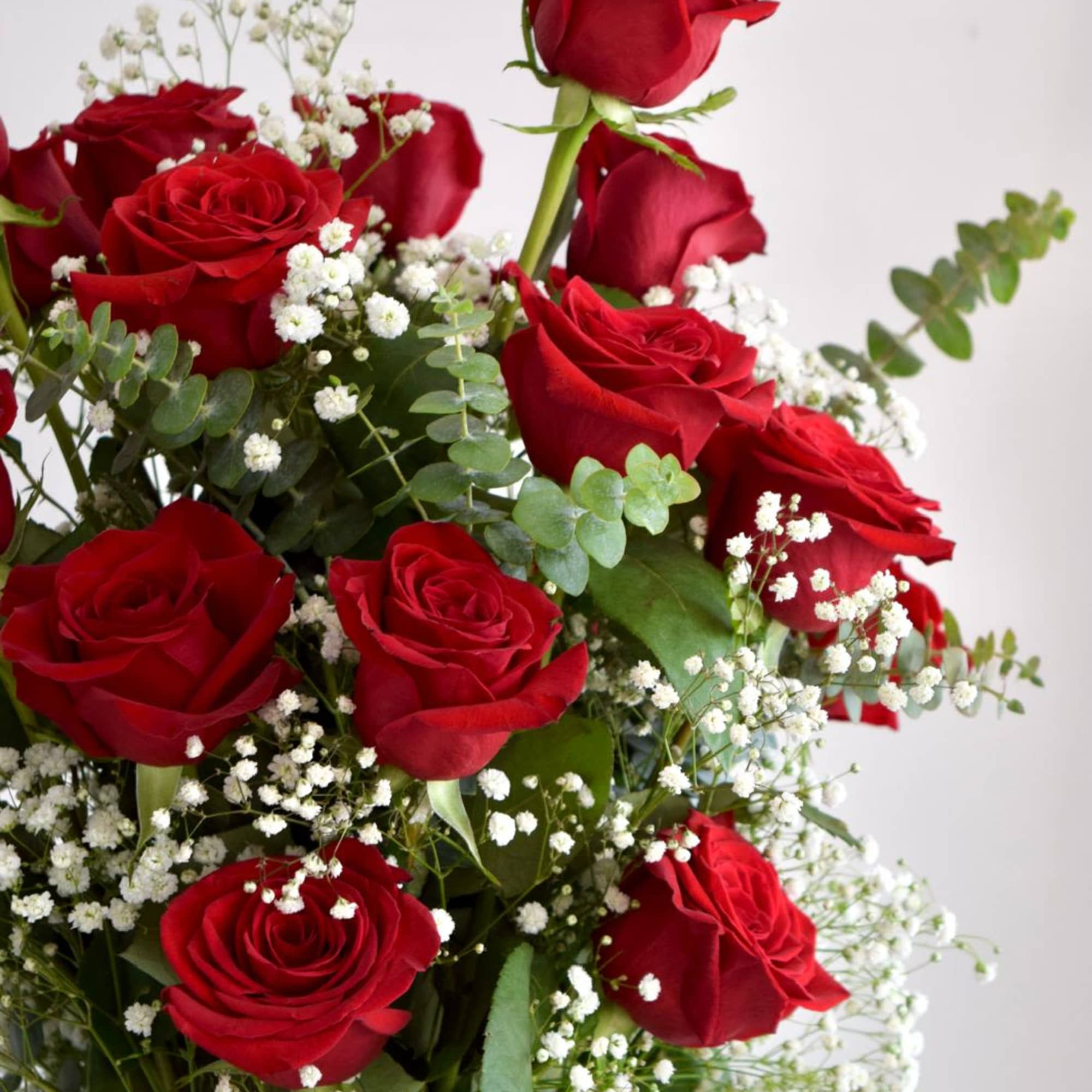 A tall cylinder glass vase with roses, eucalyptus, and baby's breath. 

Flower