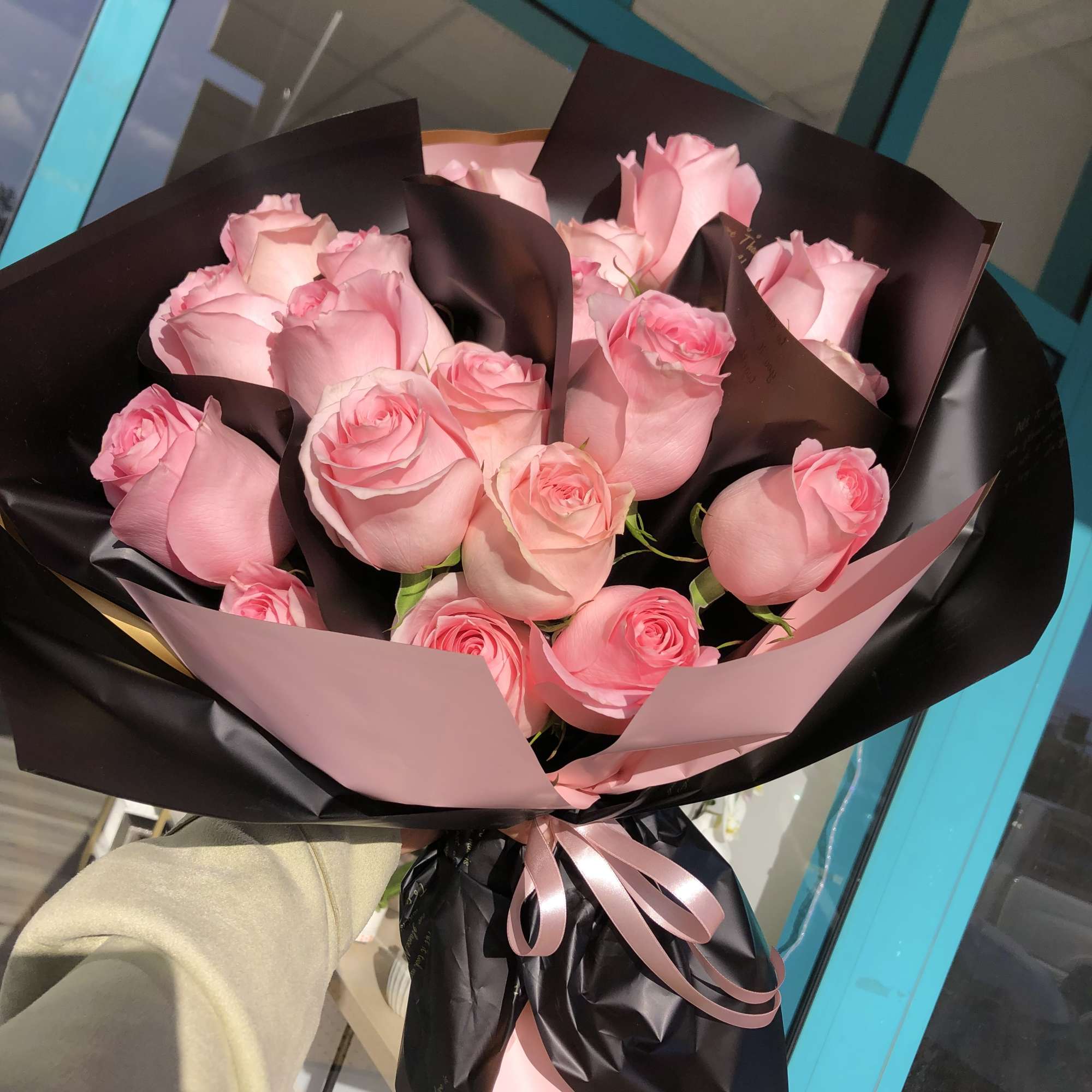 A front-facing bouquet of roses with layered paper accents, wrapped in black