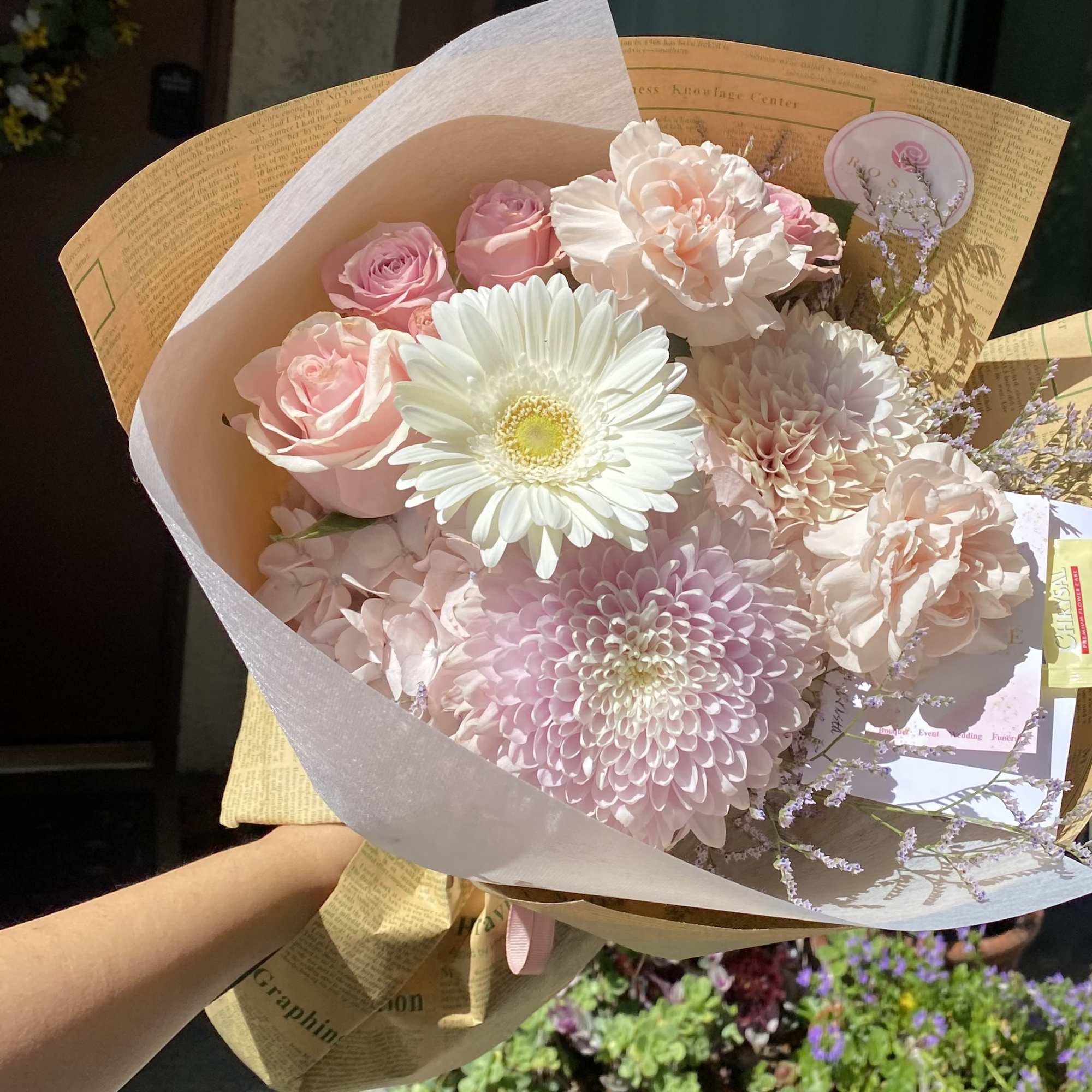 A round bouquet with pink, white, and peach flowers, wrapped in brown