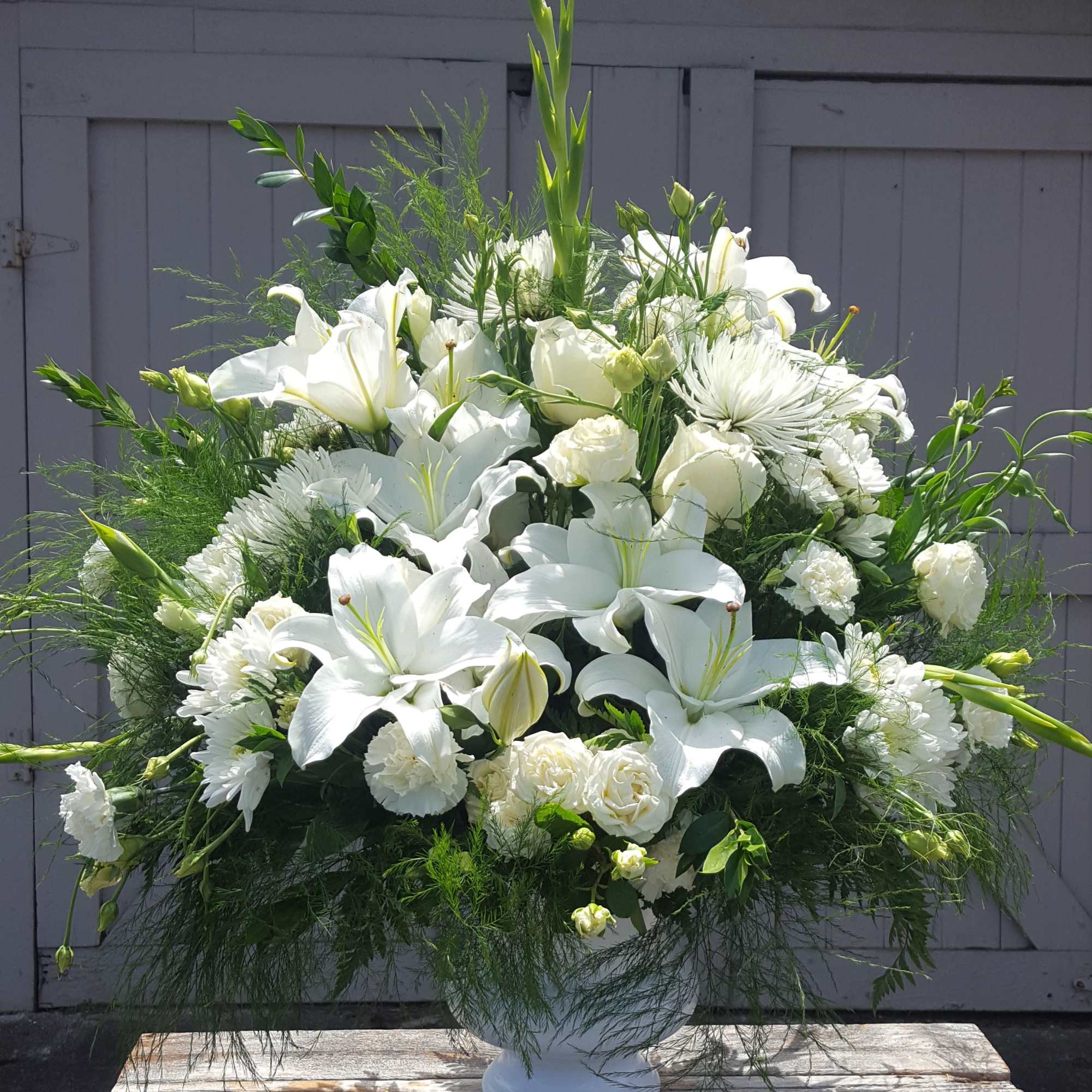 A traditional white funeral fan. Includes roses, carnations, mums, and other seasonal