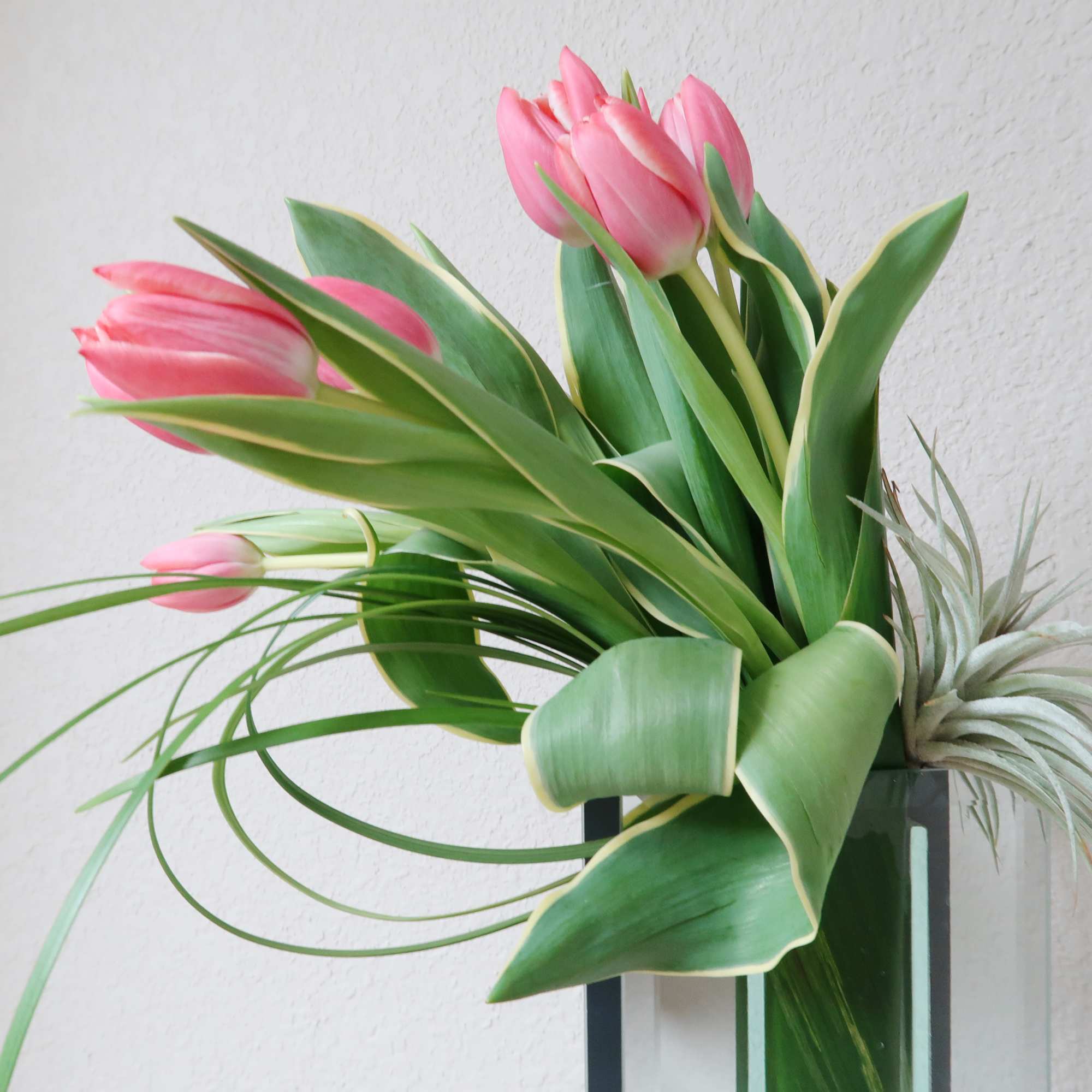 Tall mirrored vase filled with tulips accented with air plants and tropical