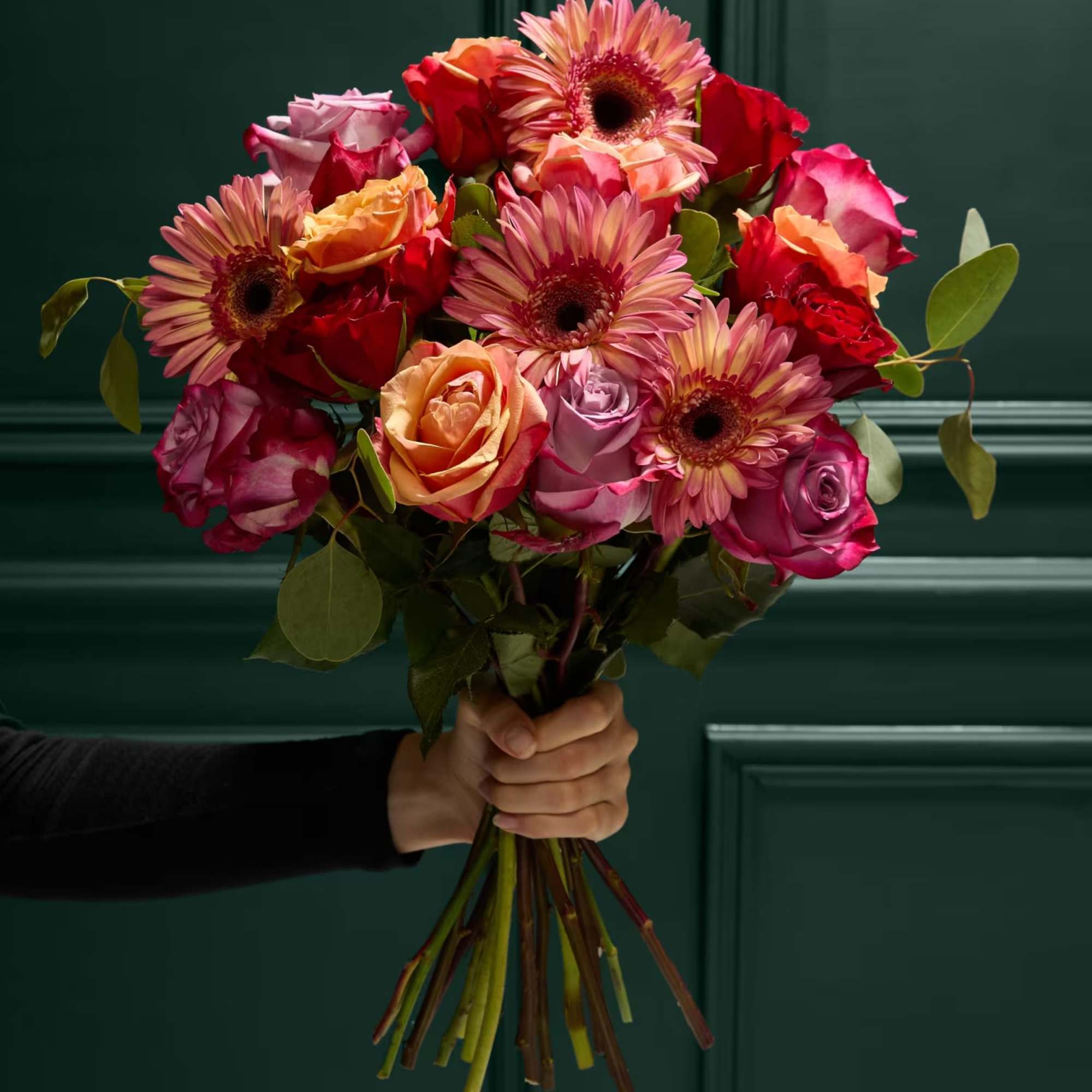 Handheld bouquet of pink and orange roses with gerbera daisies
