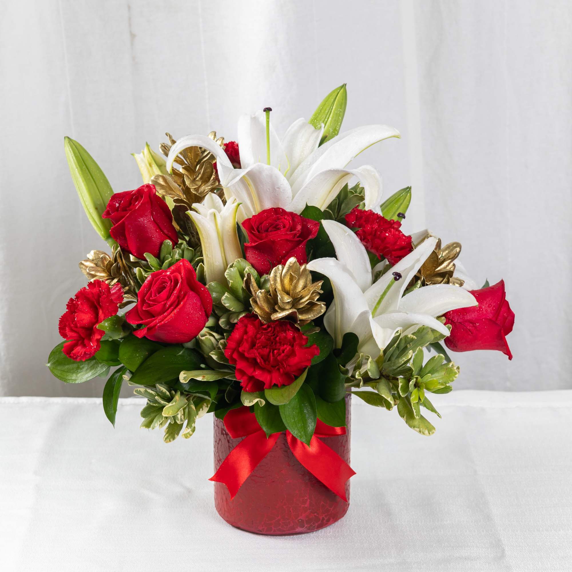 A festive blend of red roses, white lilies, and carnations, accented with