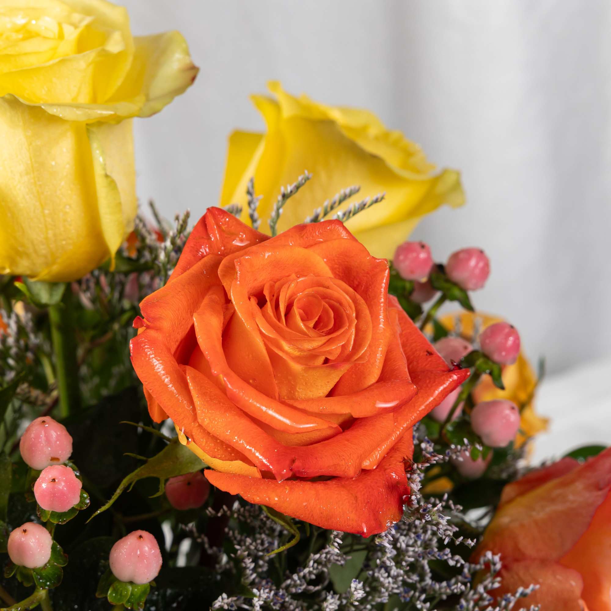 A radiant mix of yellow, orange, and pink roses with soft berries