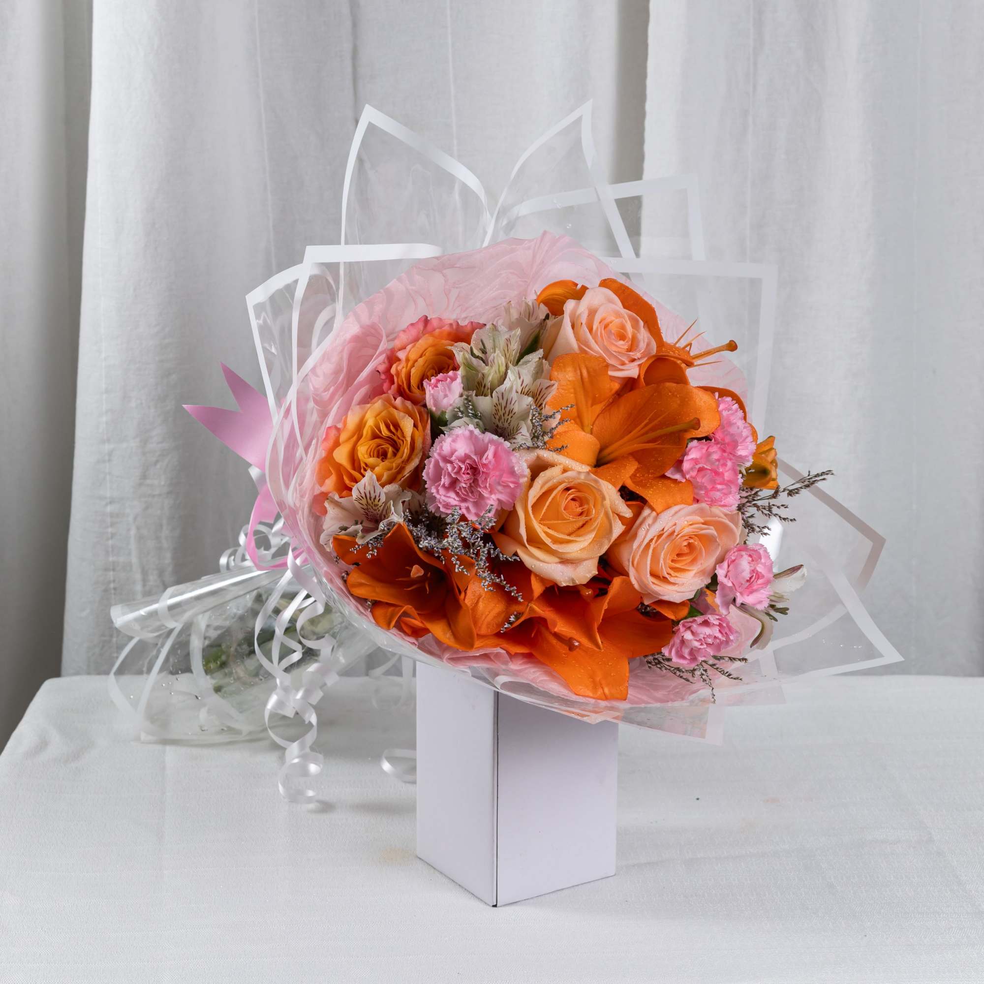 A delicate bouquet of orange roses and soft pink carnations, wrapped in