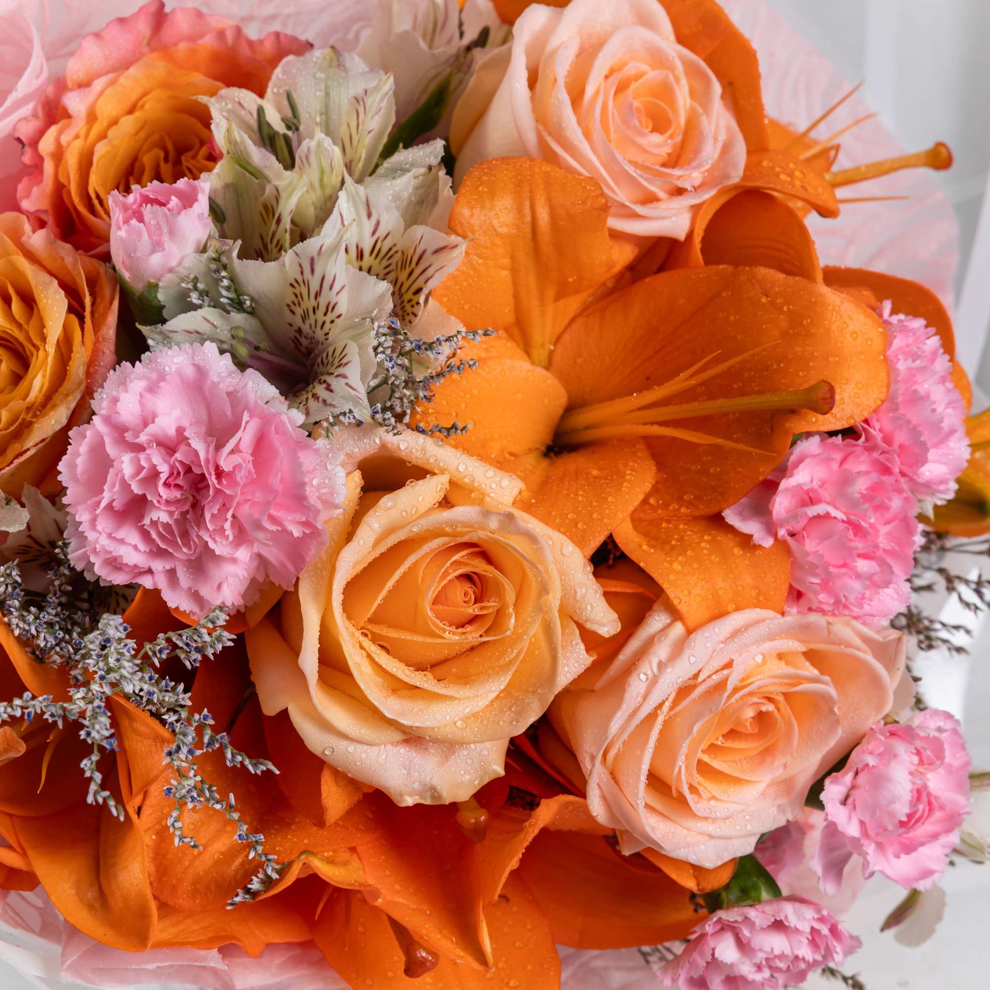 A delicate bouquet of orange roses and soft pink carnations, wrapped in
