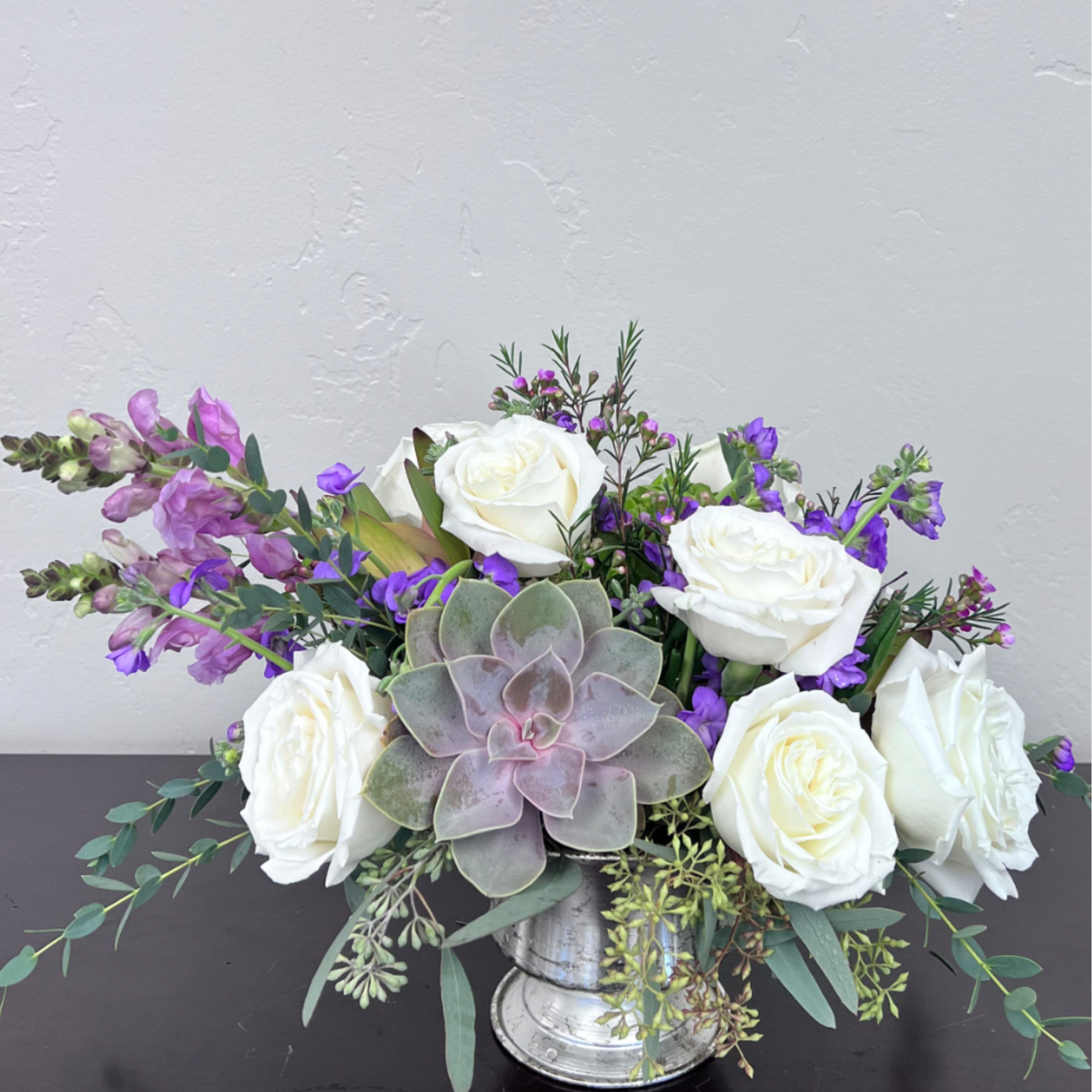 Creamy white roses are artfully arranged with delicate purple accents, textured foliage