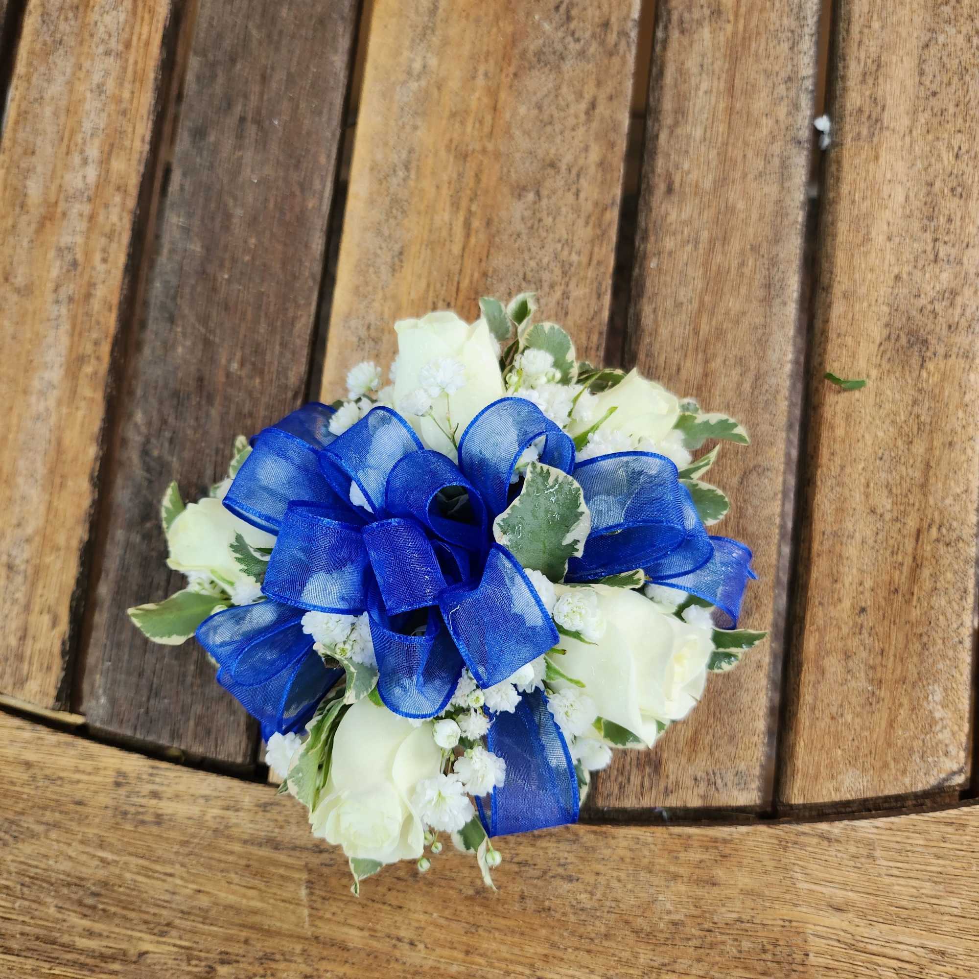 Wrist corsage with white spray roses, filler, greenery and royal blue ribbon.