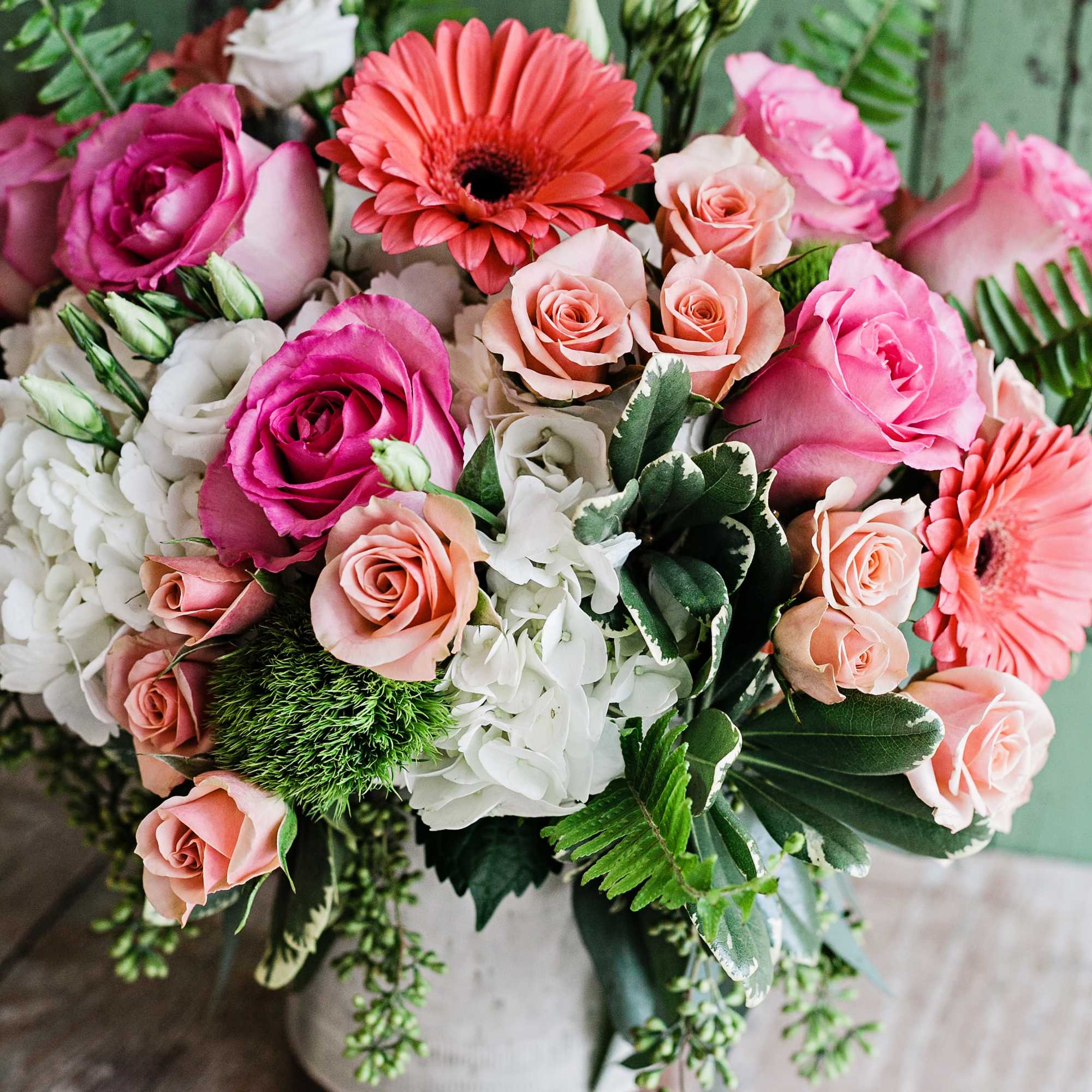 A ceramic white crock featuring hydrangeas, roses, gerbera daisy and lisianthus with