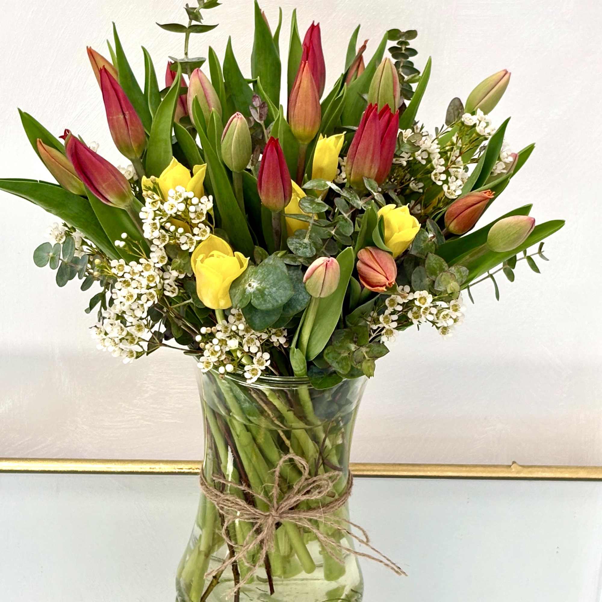 Glass vase of red and peach tulips with yellow roses and small white blossoms.