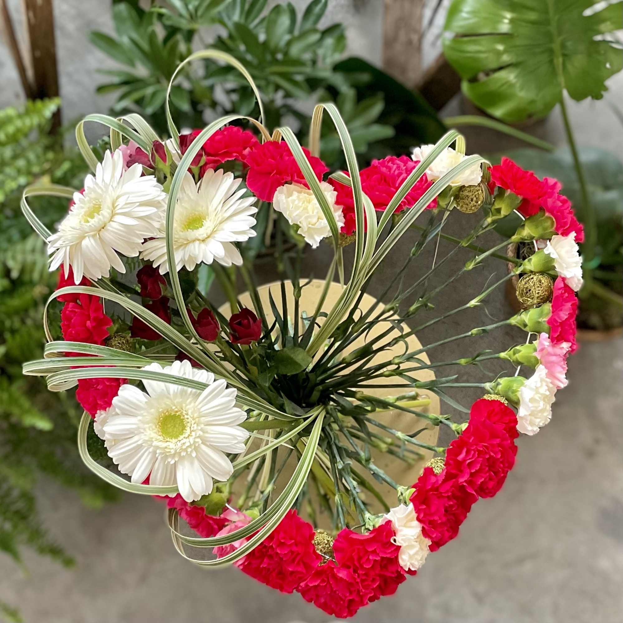 Carnations are skillfully arranged into a heart shape, accented with a gerbera