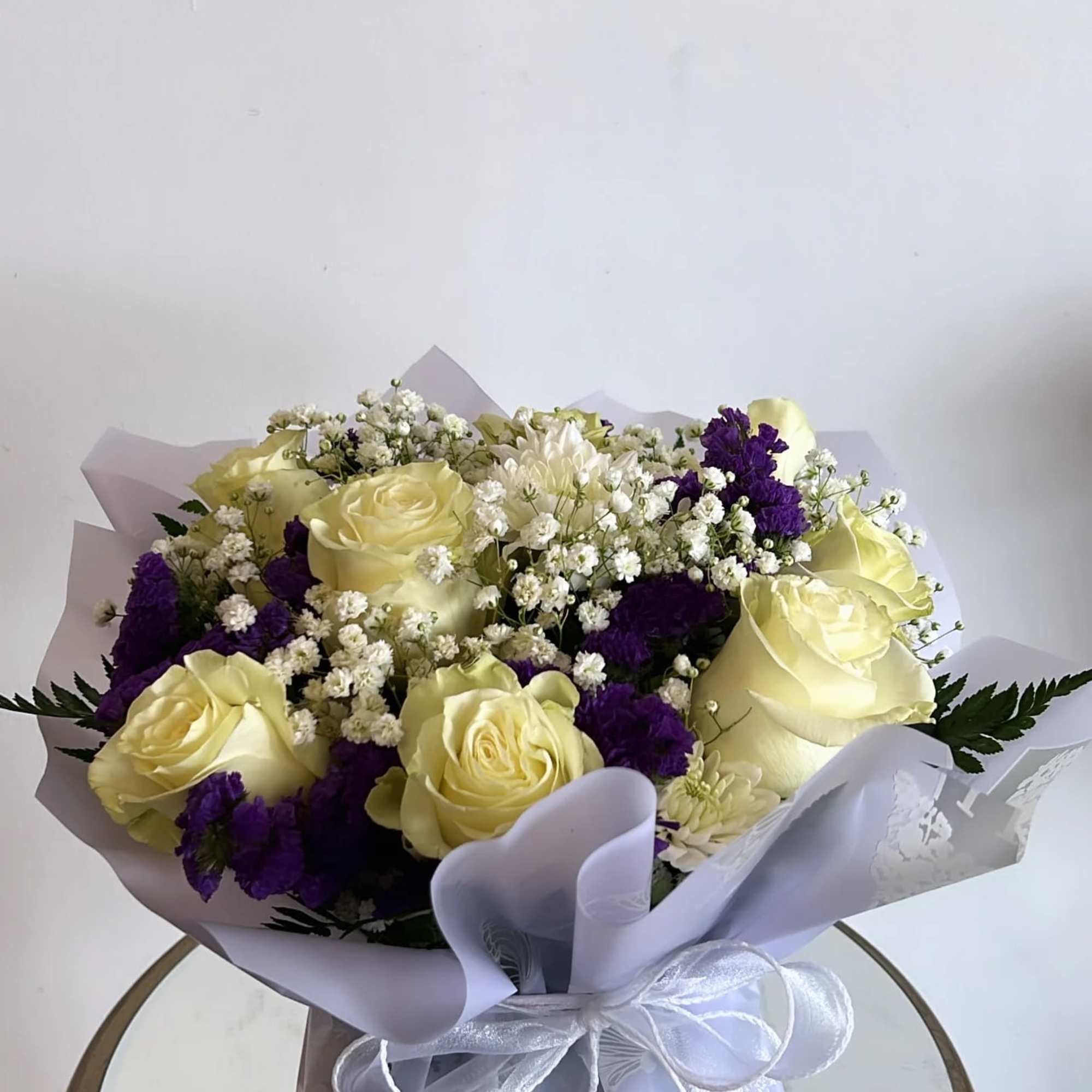 -The bouquet is composed primarily of delicate white roses, purple statice and