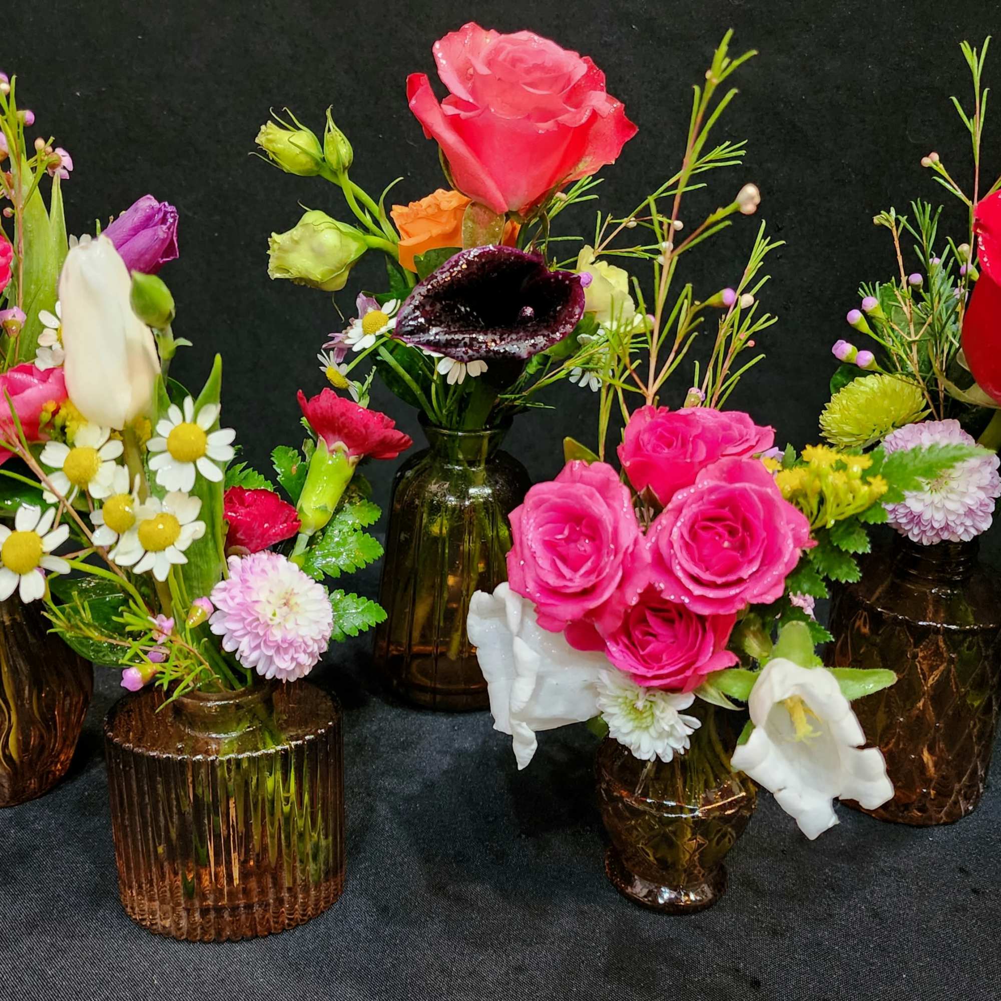 An eclectic assortment of flowers in brown vintage bud vases for those