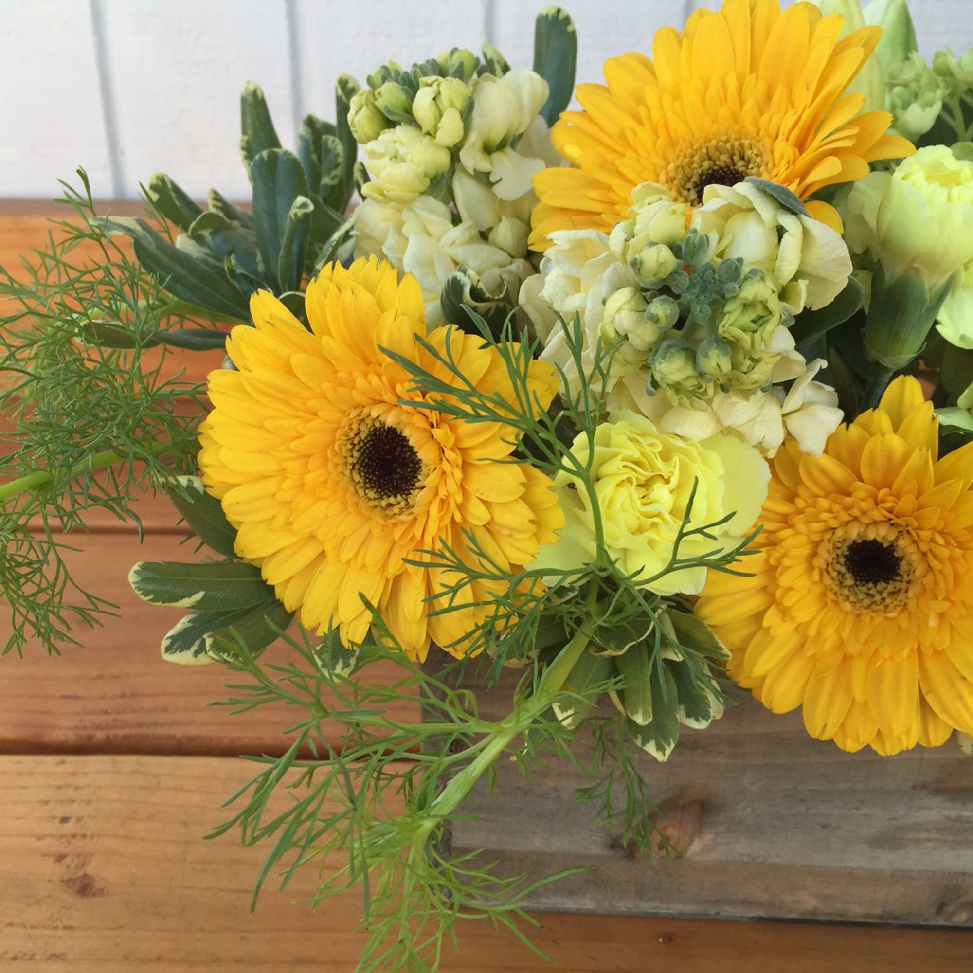 Low wooden box arrangement with yellow gerbera daisies and soft yellow blooms