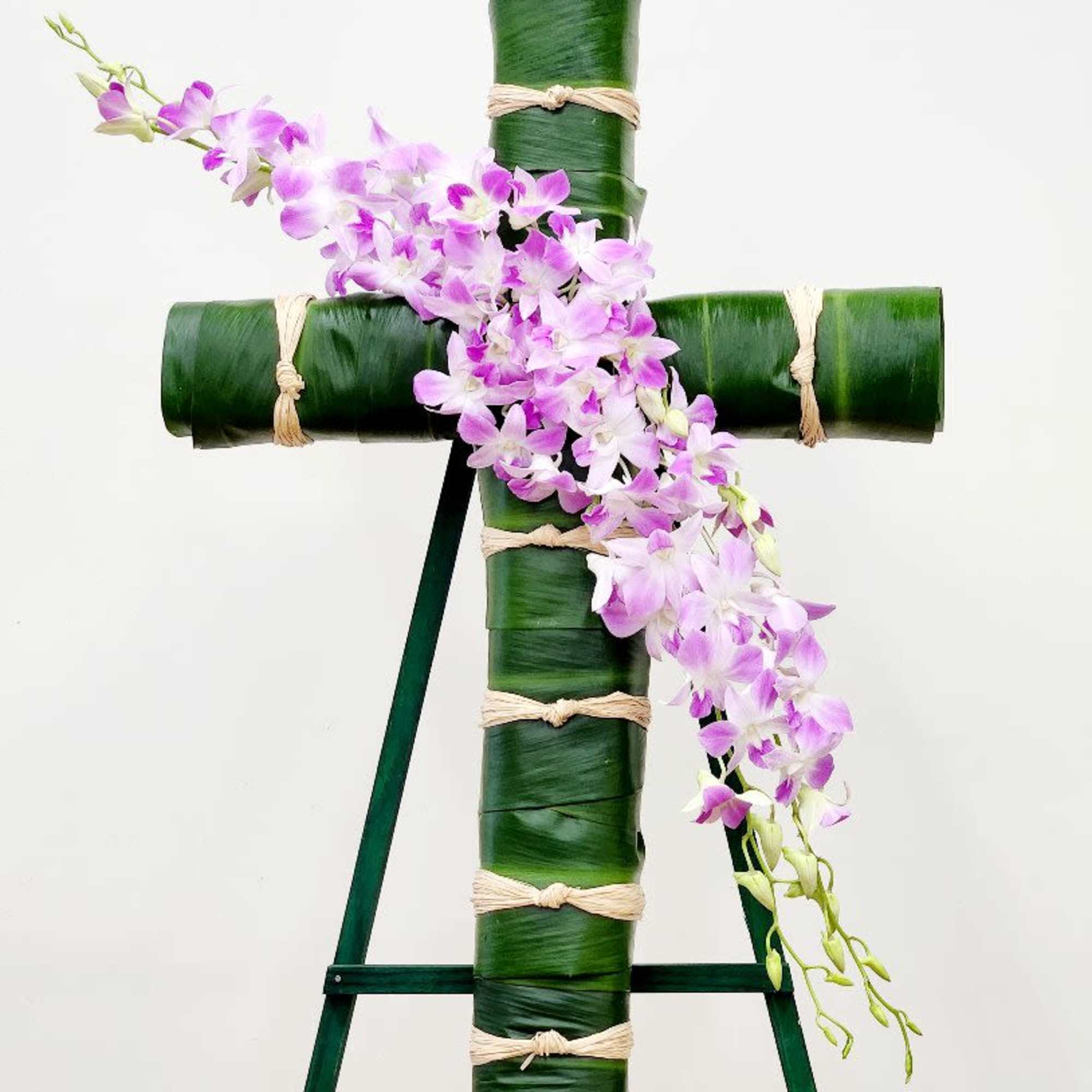 A striking tribute arrangement featuring a cross form wrapped in verdant ti