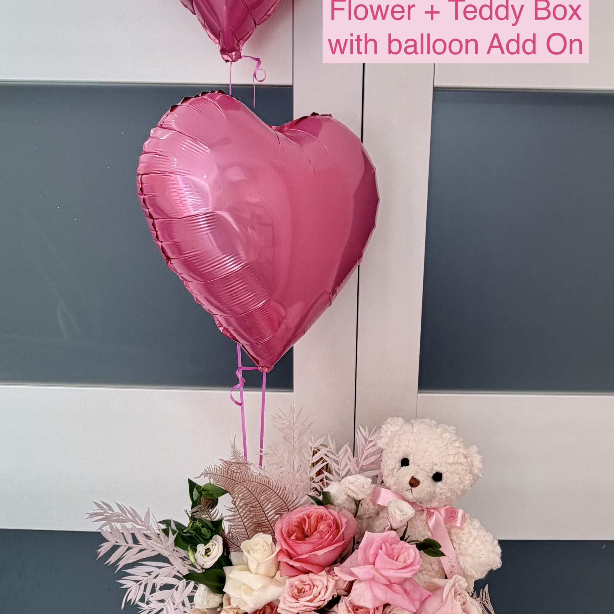 Pink heart balloons above a pink rose arrangement with a teddy bear