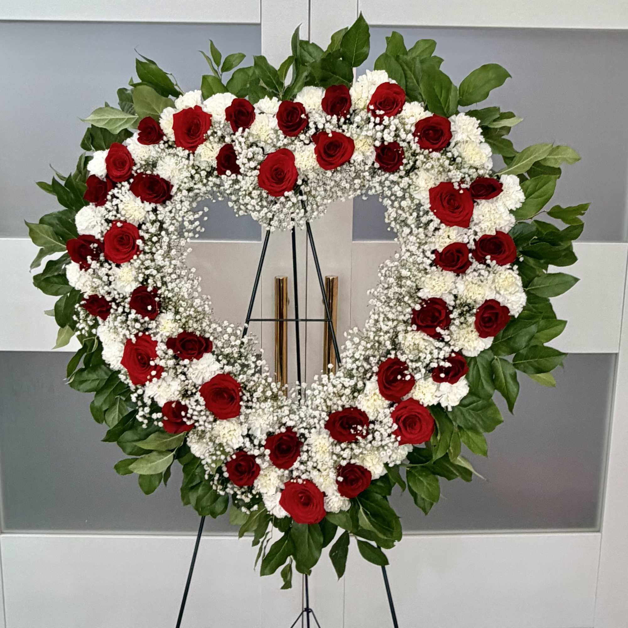 Heart-shaped floral wreath with red roses and white flowers on an easel