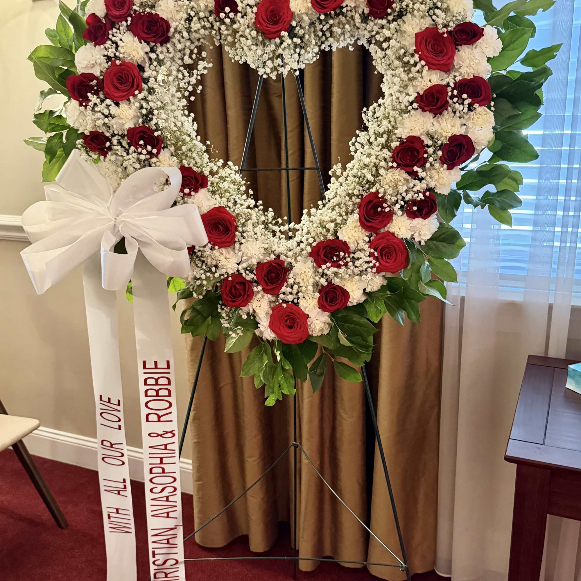 Heart-shaped red rose wreath on an easel with white ribbon
