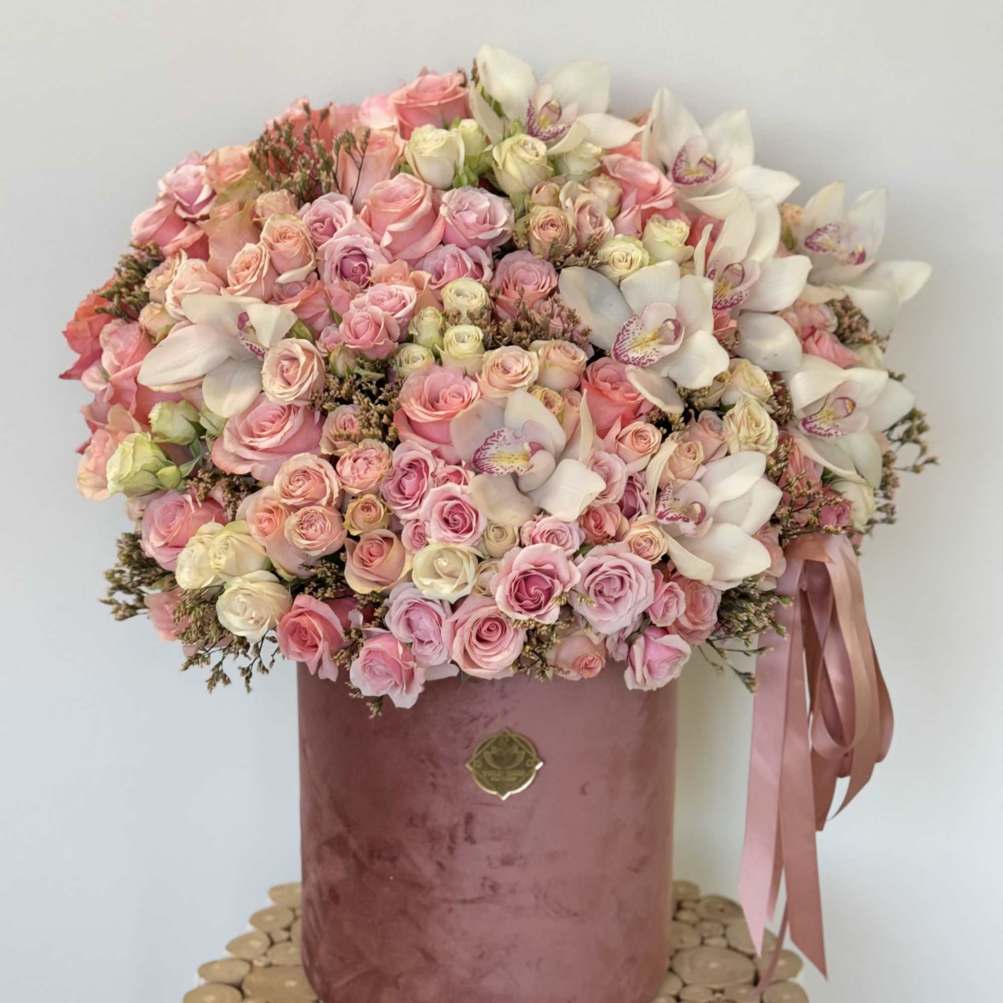 This luxurious arrangement of blush pink roses, delicate orchids, and soft accents
