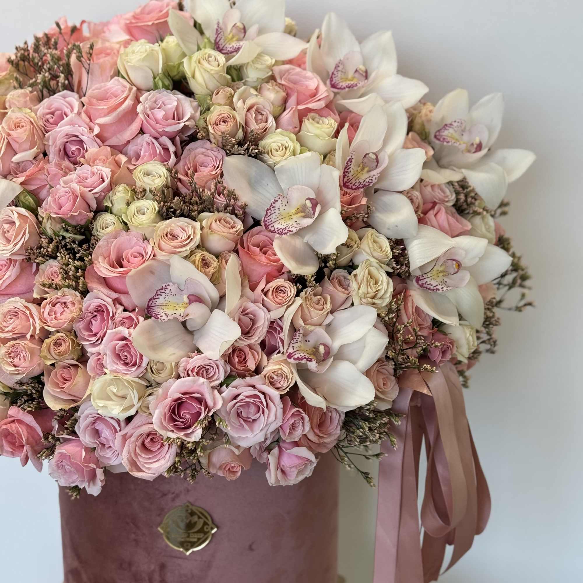 This luxurious arrangement of blush pink roses, delicate orchids, and soft accents