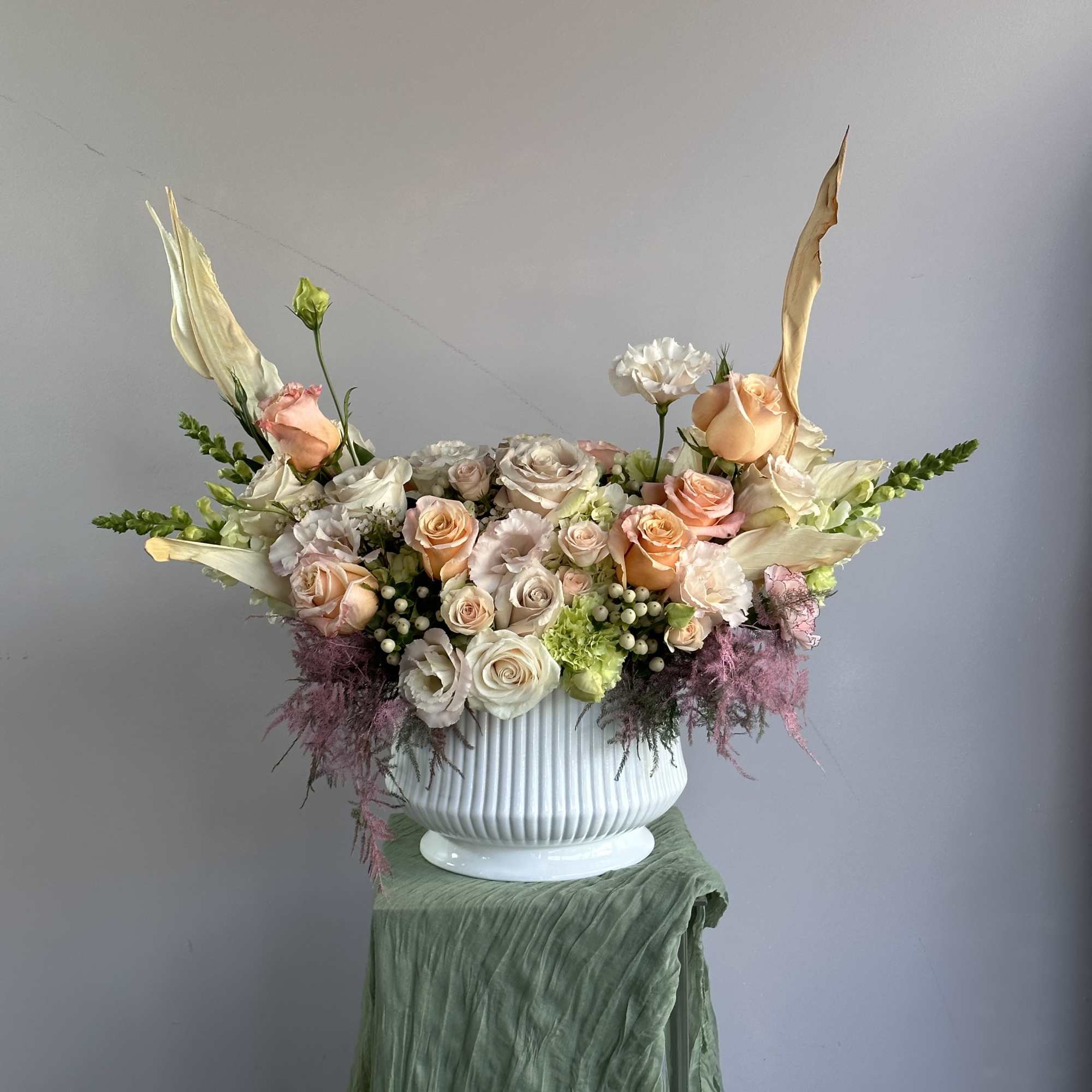 This elegant floral arrangement features soft peach and blush roses, complemented by