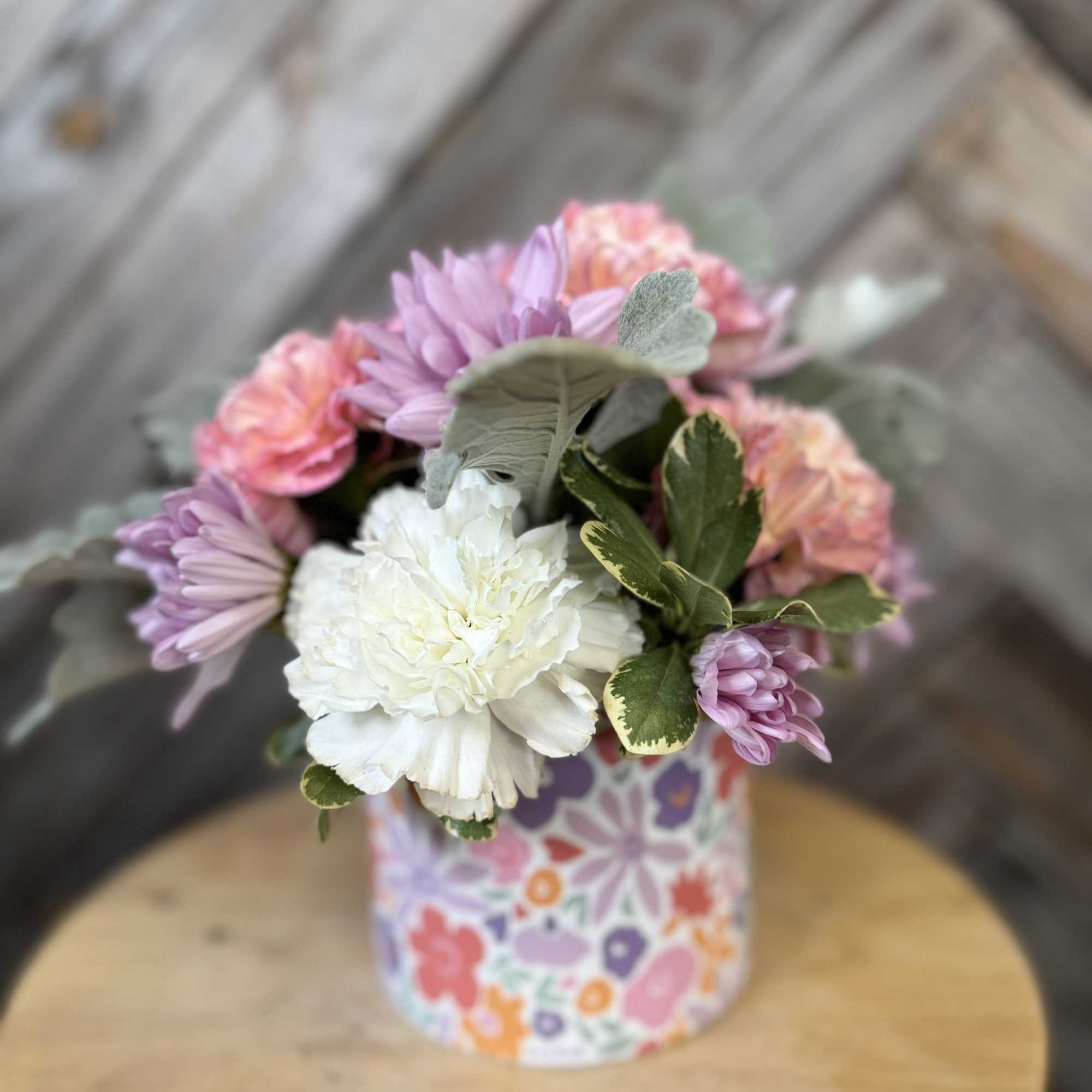Small bouquet of pink, lavender, and white flowers in a patterned container