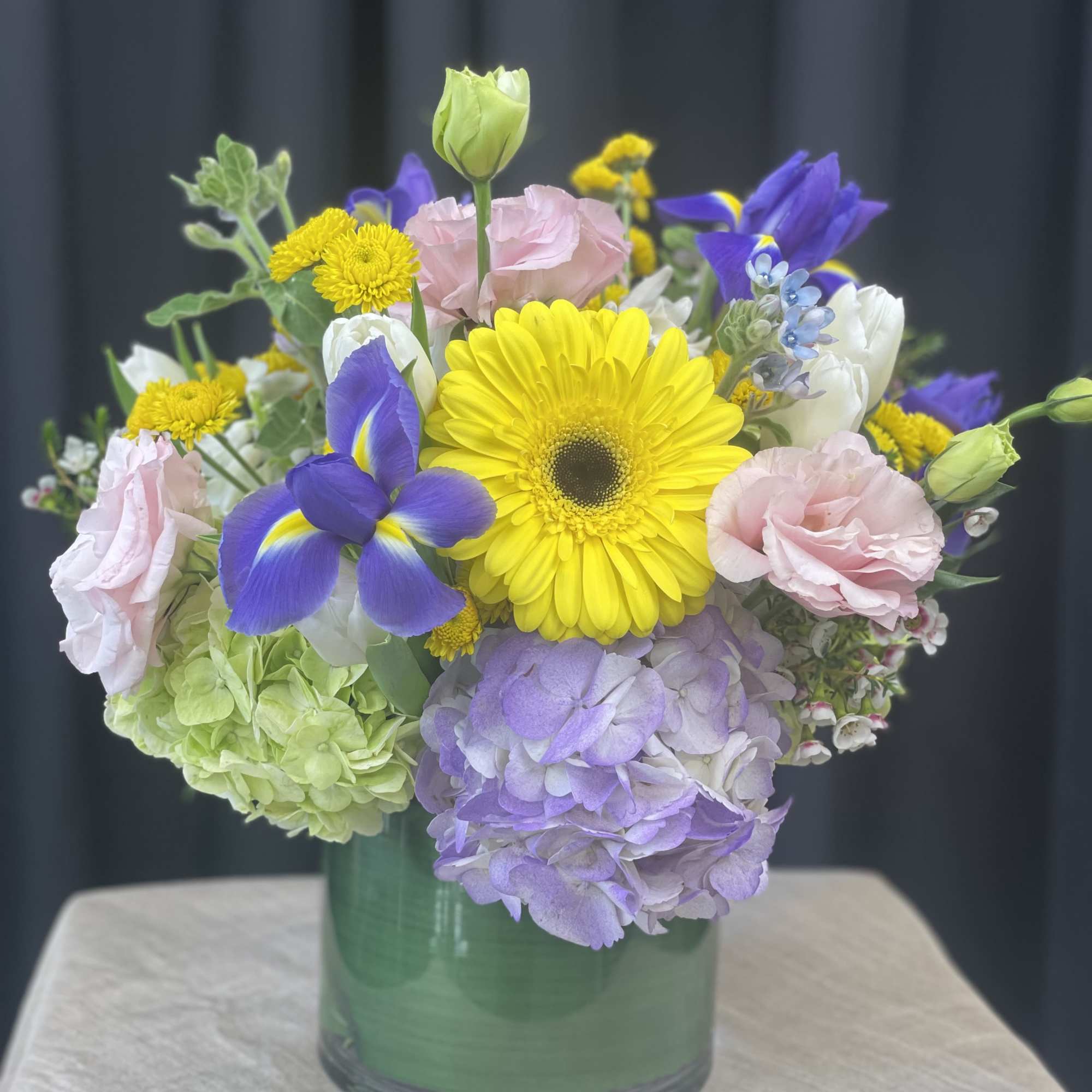 Mixed bouquet in a green glass vase with yellow, purple, pink, and white blooms