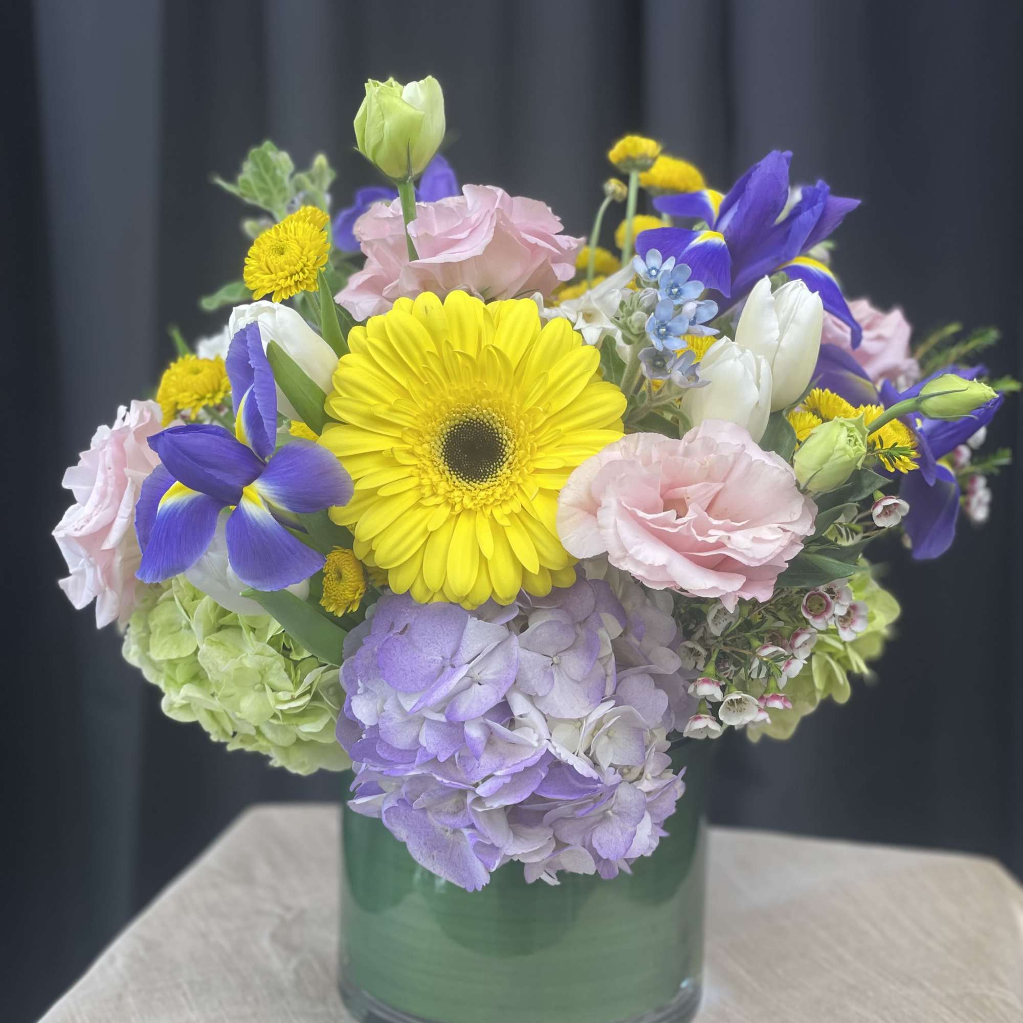 Mixed bouquet with yellow gerbera daisies, pink roses, and purple irises in a glass vase
