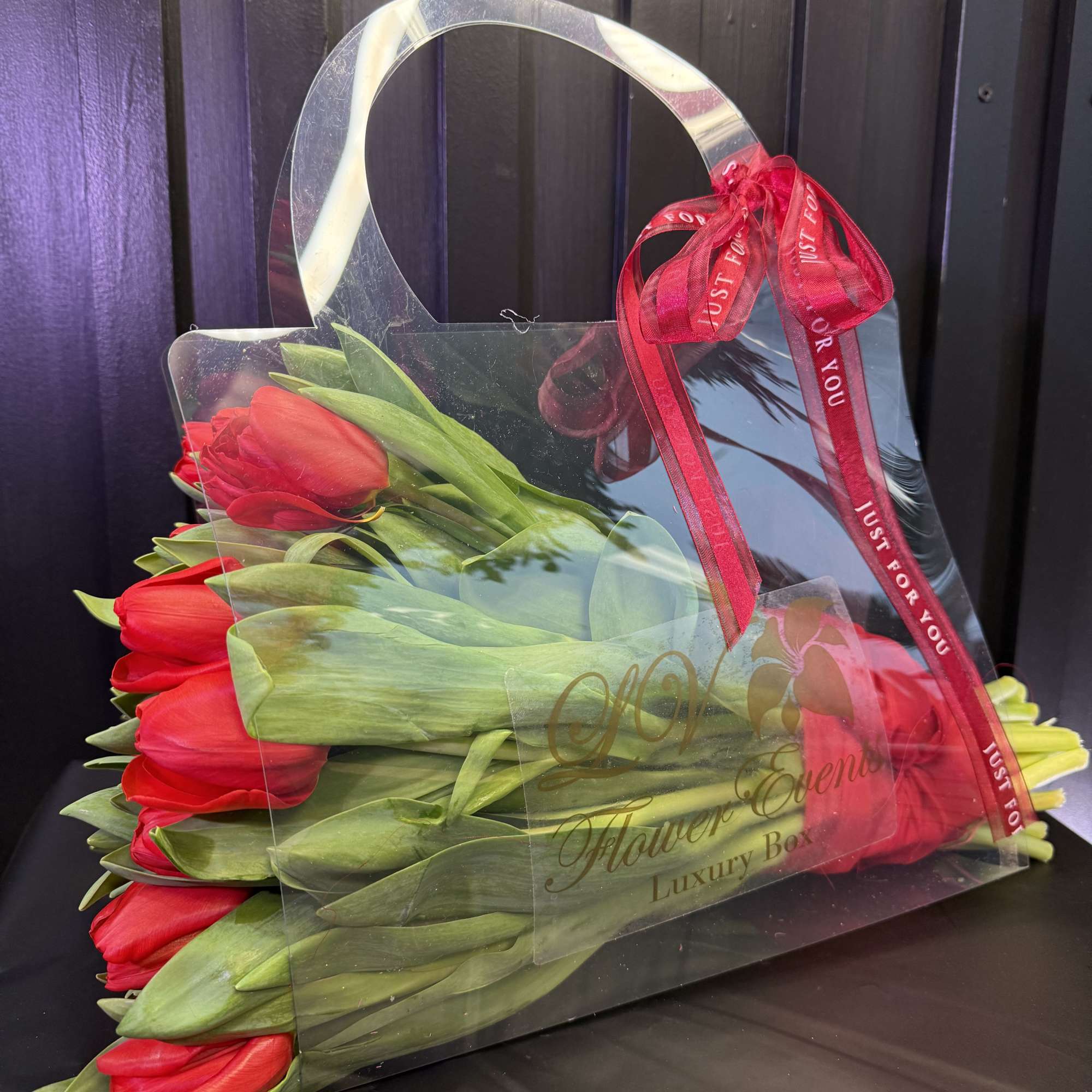 Red tulips arranged in a clear handled gift box with a ribbon bow