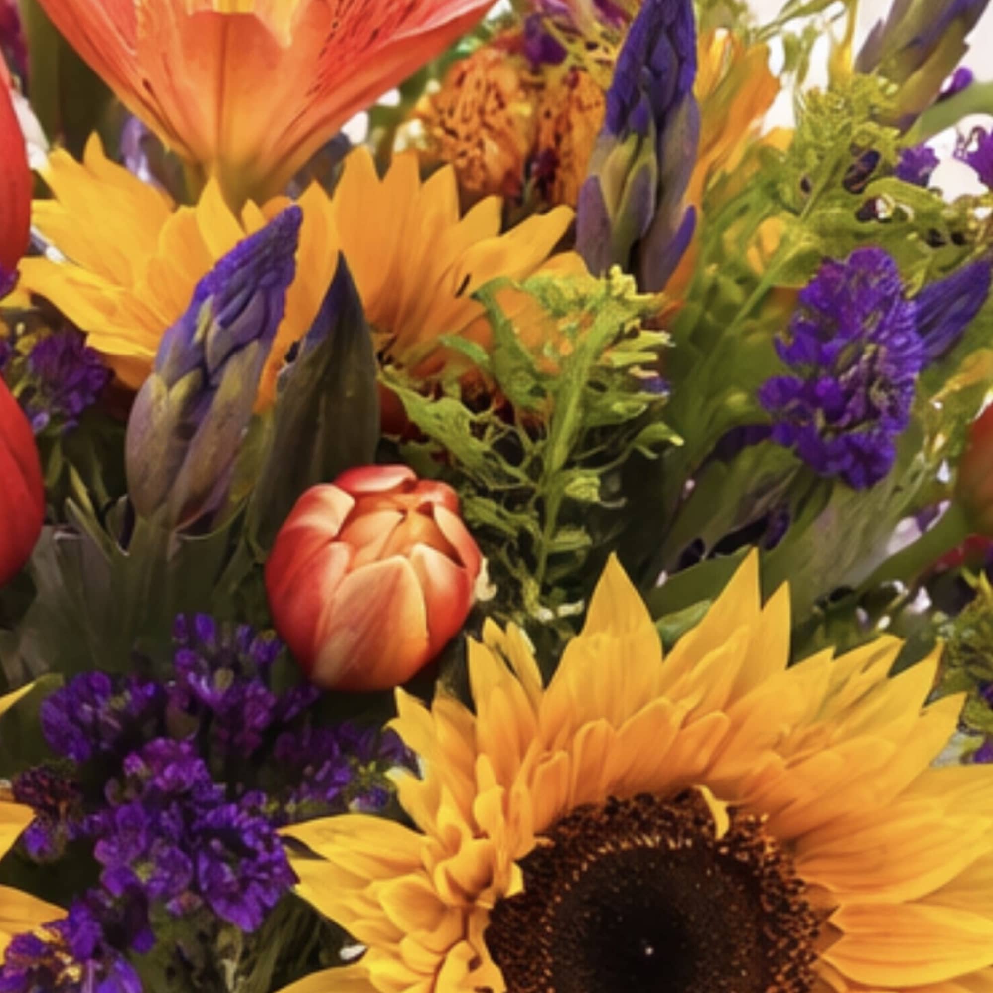 This colorful arrangement comes complete with sunflowers, statice, tulips, lilies, solidago, irises