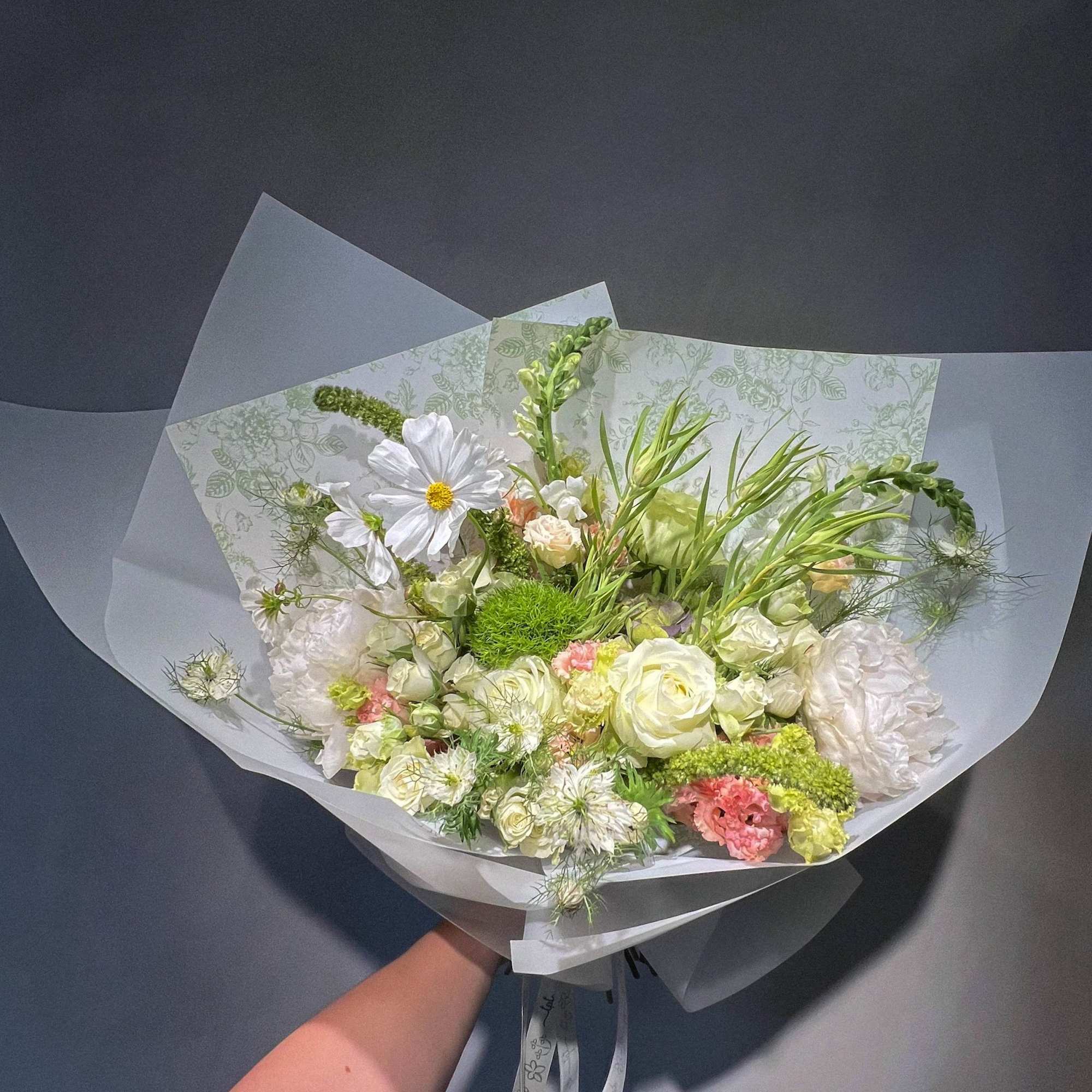 Handheld bouquet of white and pale green flowers wrapped in translucent paper