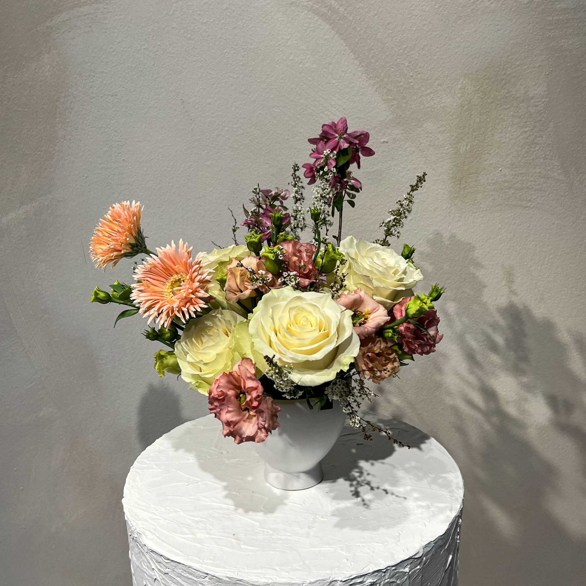 Mixed bouquet of cream roses and peach flowers in a white vase