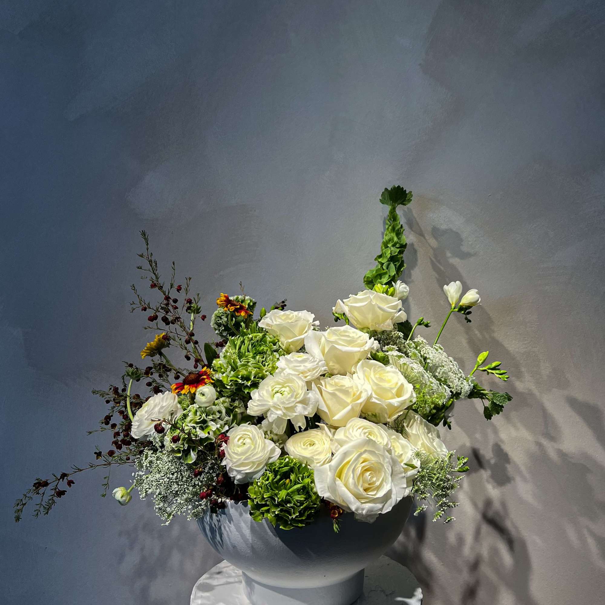 White roses and green flowers arranged in a round vase