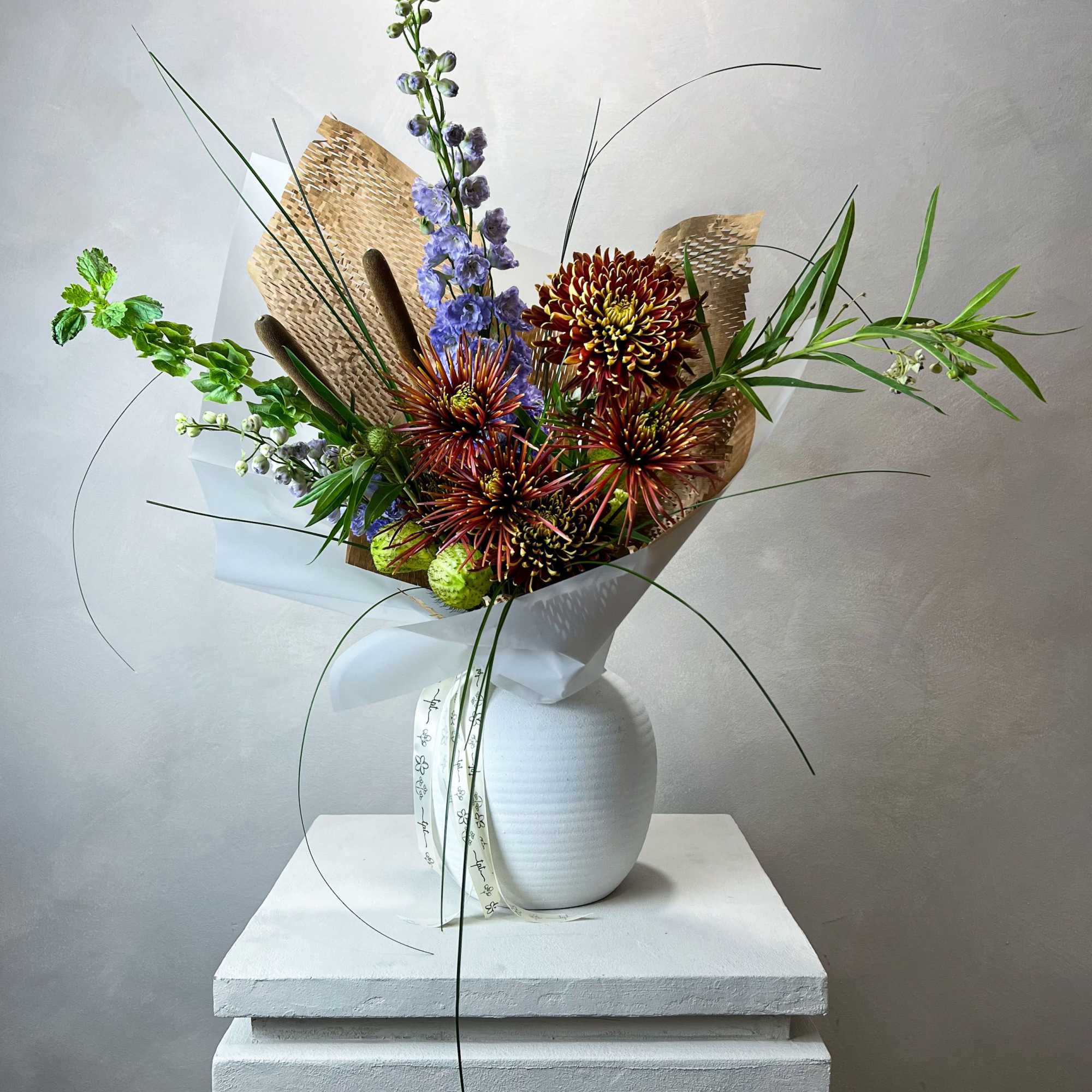 Tall bouquet of chrysanthemums and blue delphinium in a white vase