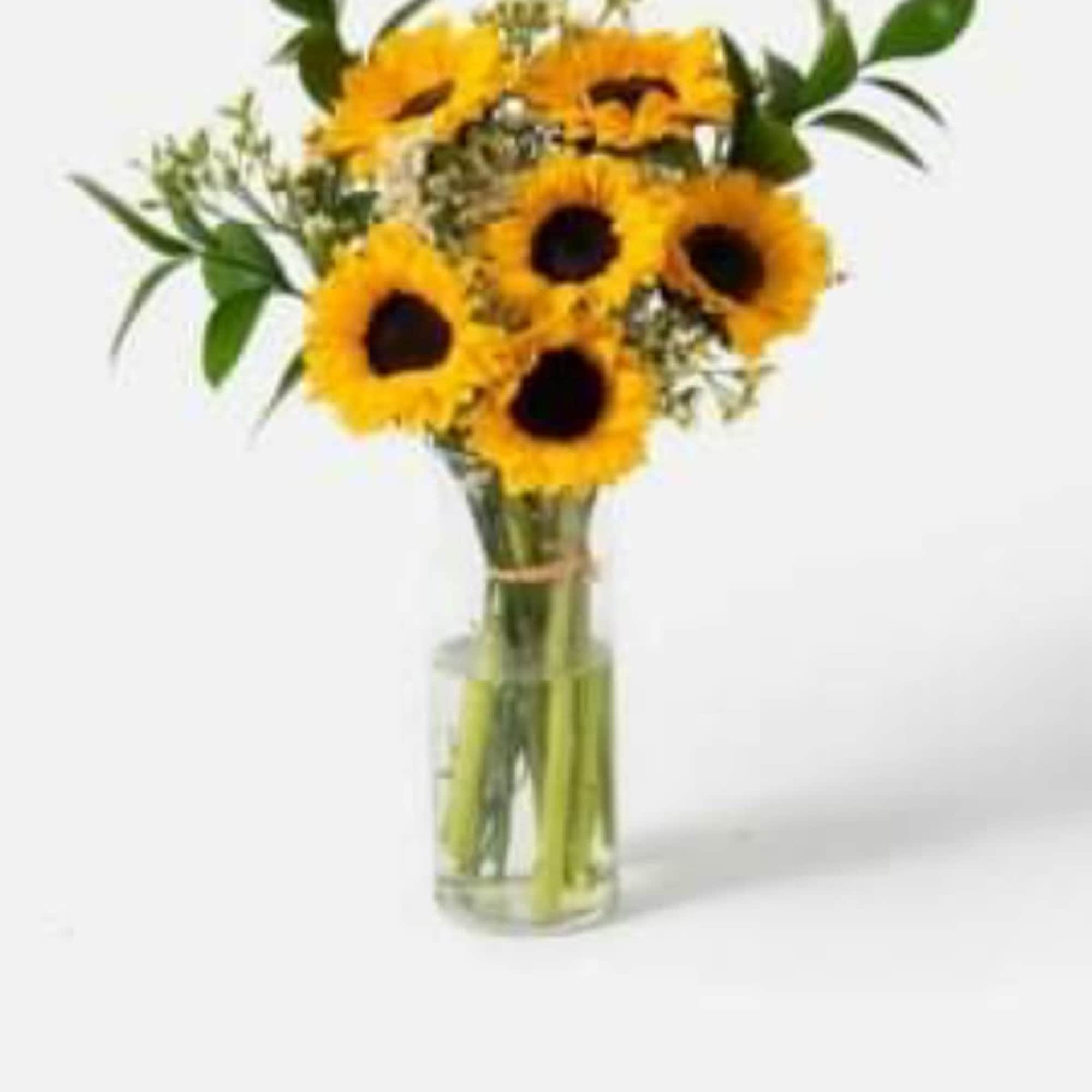 Sunflowers and a variety of greens in a glass vase. 