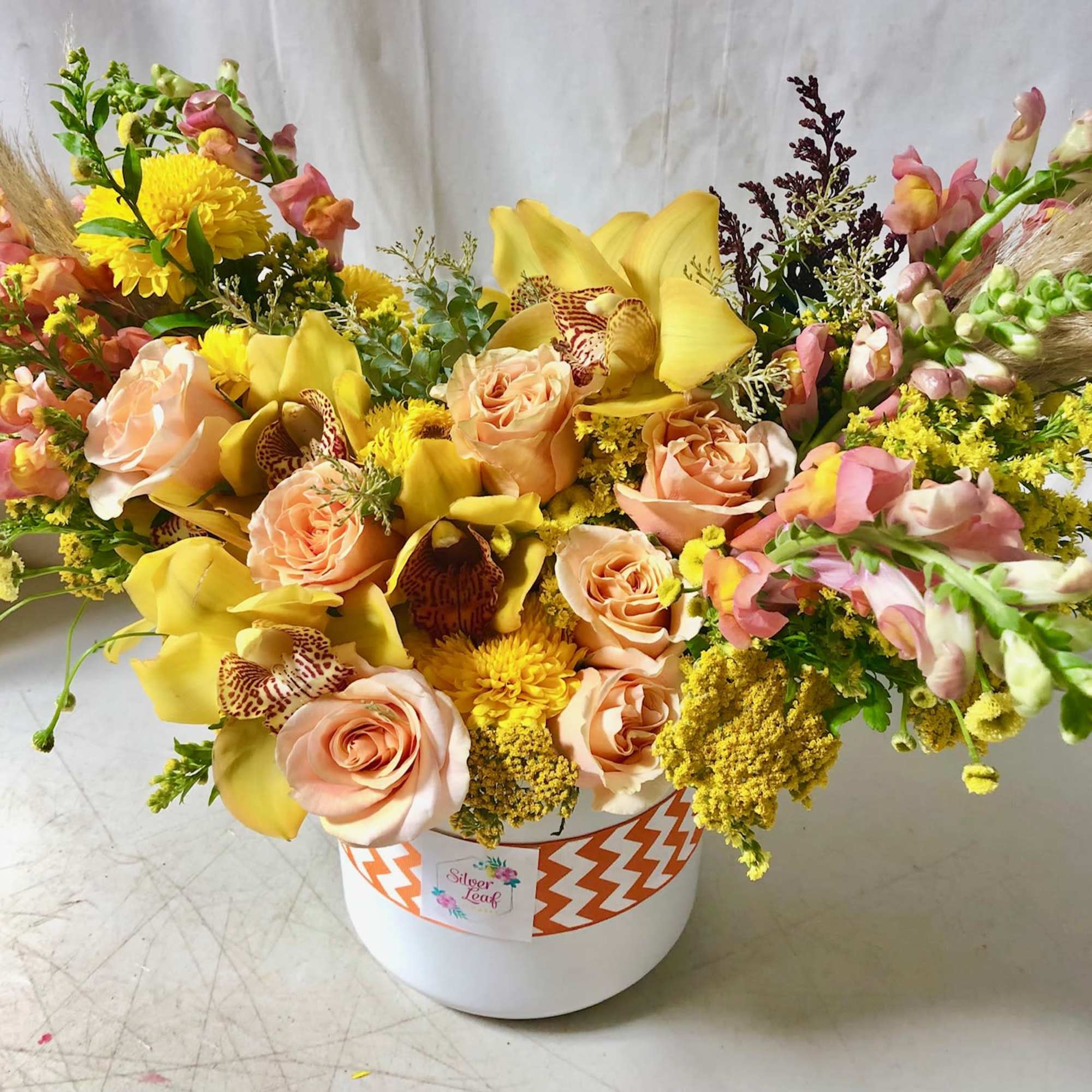 Peach roses and yellow orchids in a white hat box